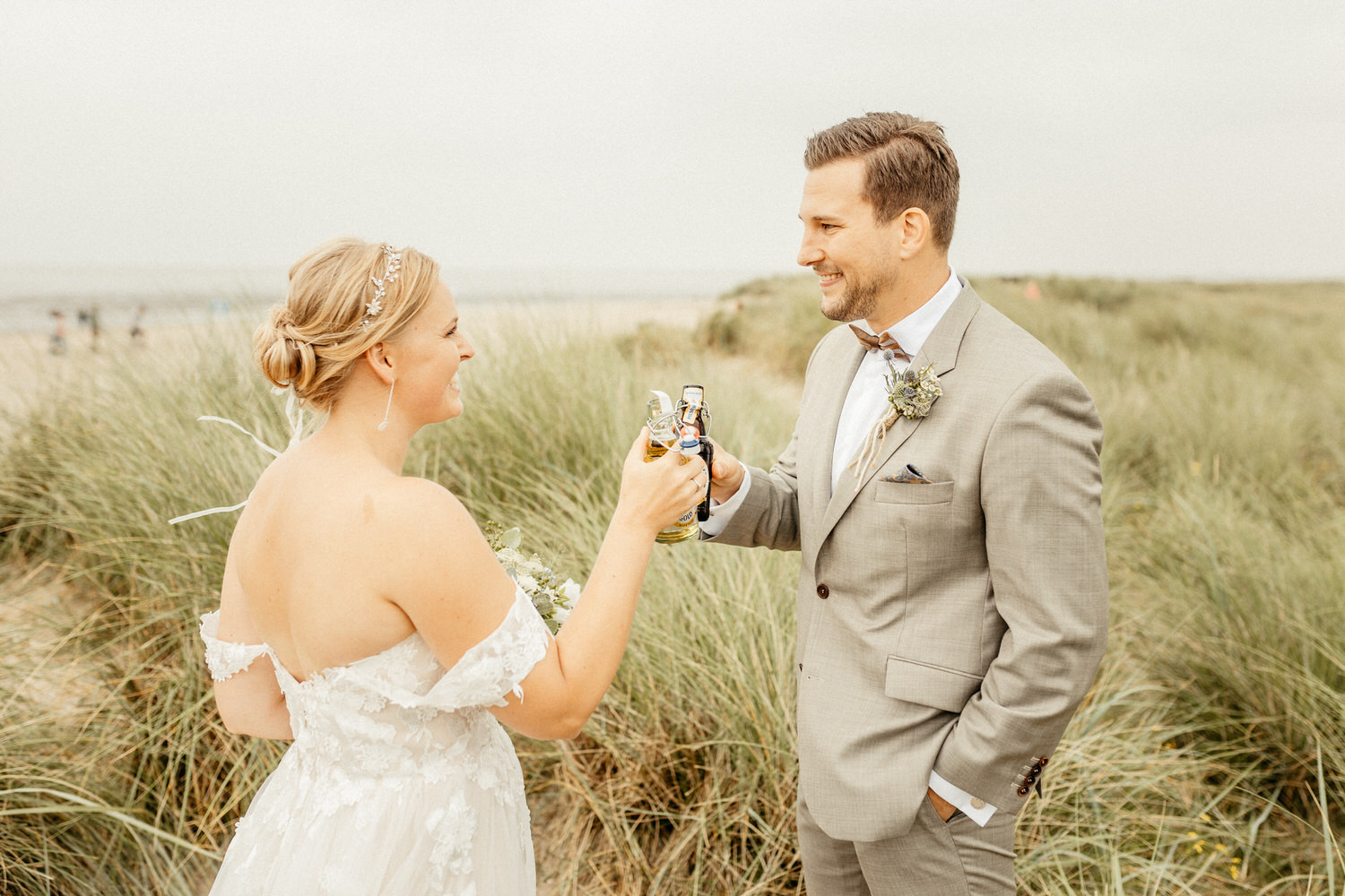 Braut und Bräutigam stoßen mit Bier an in den Dünen