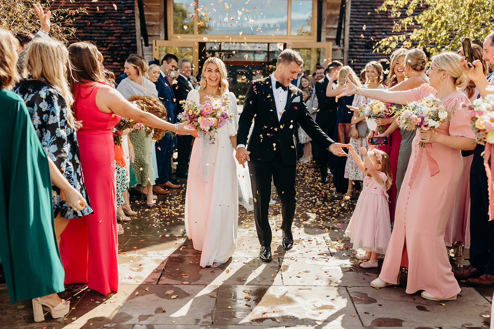 Newlyweds walking through a courtyard as colourful confetti flutters behind them at their Silchester Farm wedding.