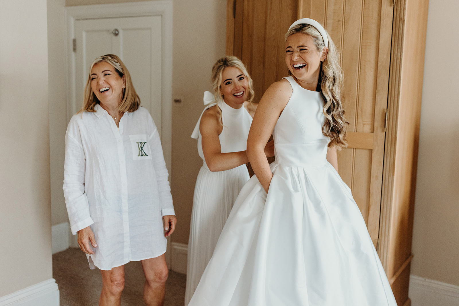 bride laughing with mother and sister as she gets in her wedding dress