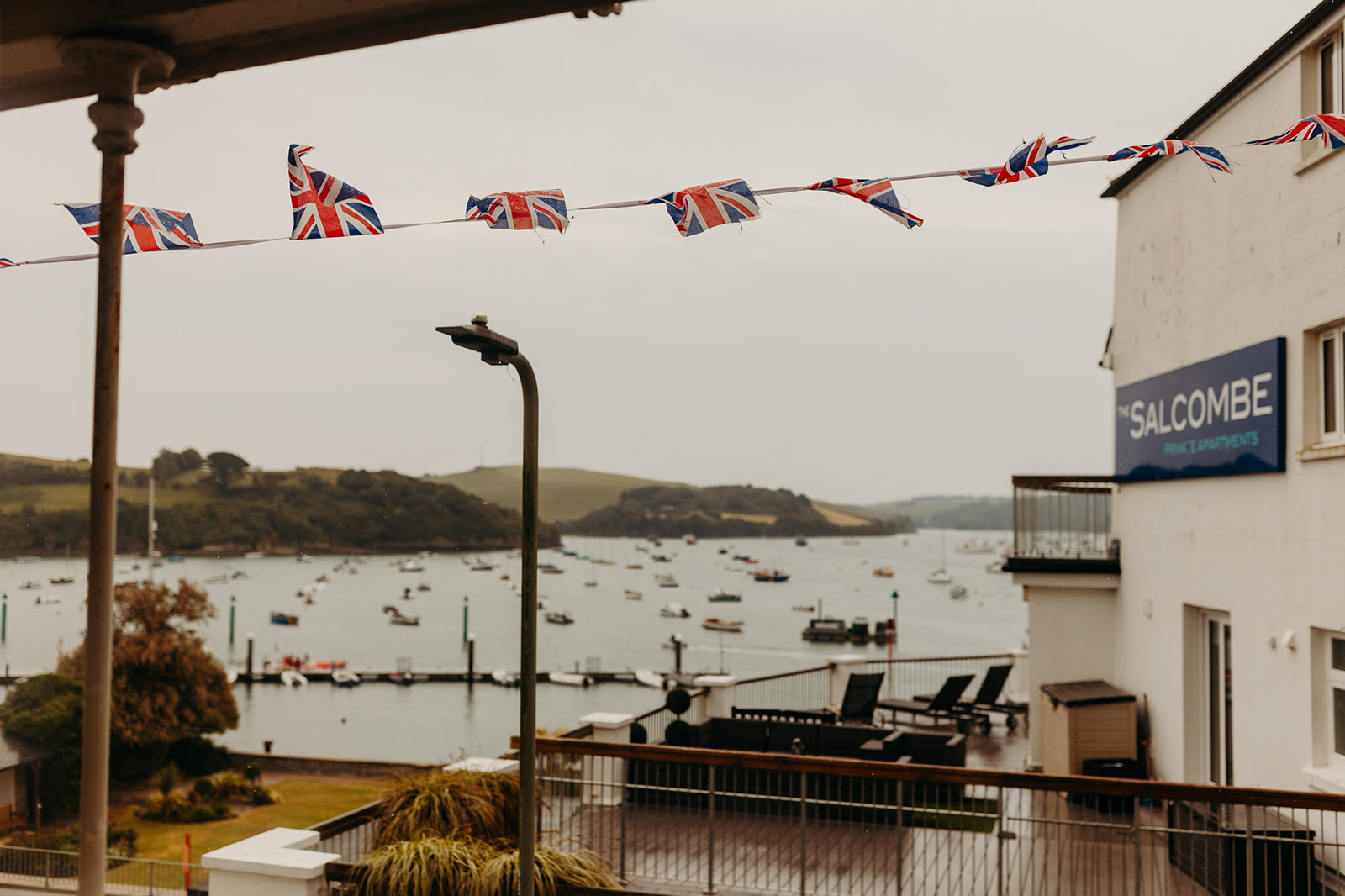 Salcombe on morning of a misty wedding, british flags wave in foreground, boats dot the water landscape in background
