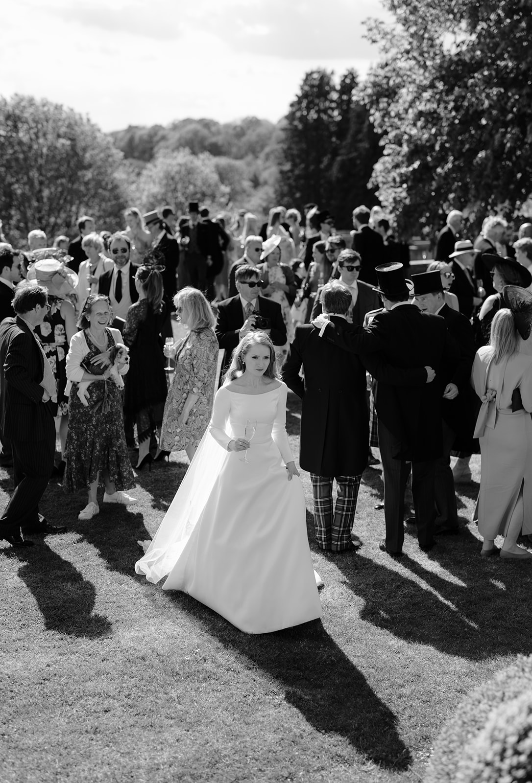 Bride walking through gardens as guests enjoy the drinks reception