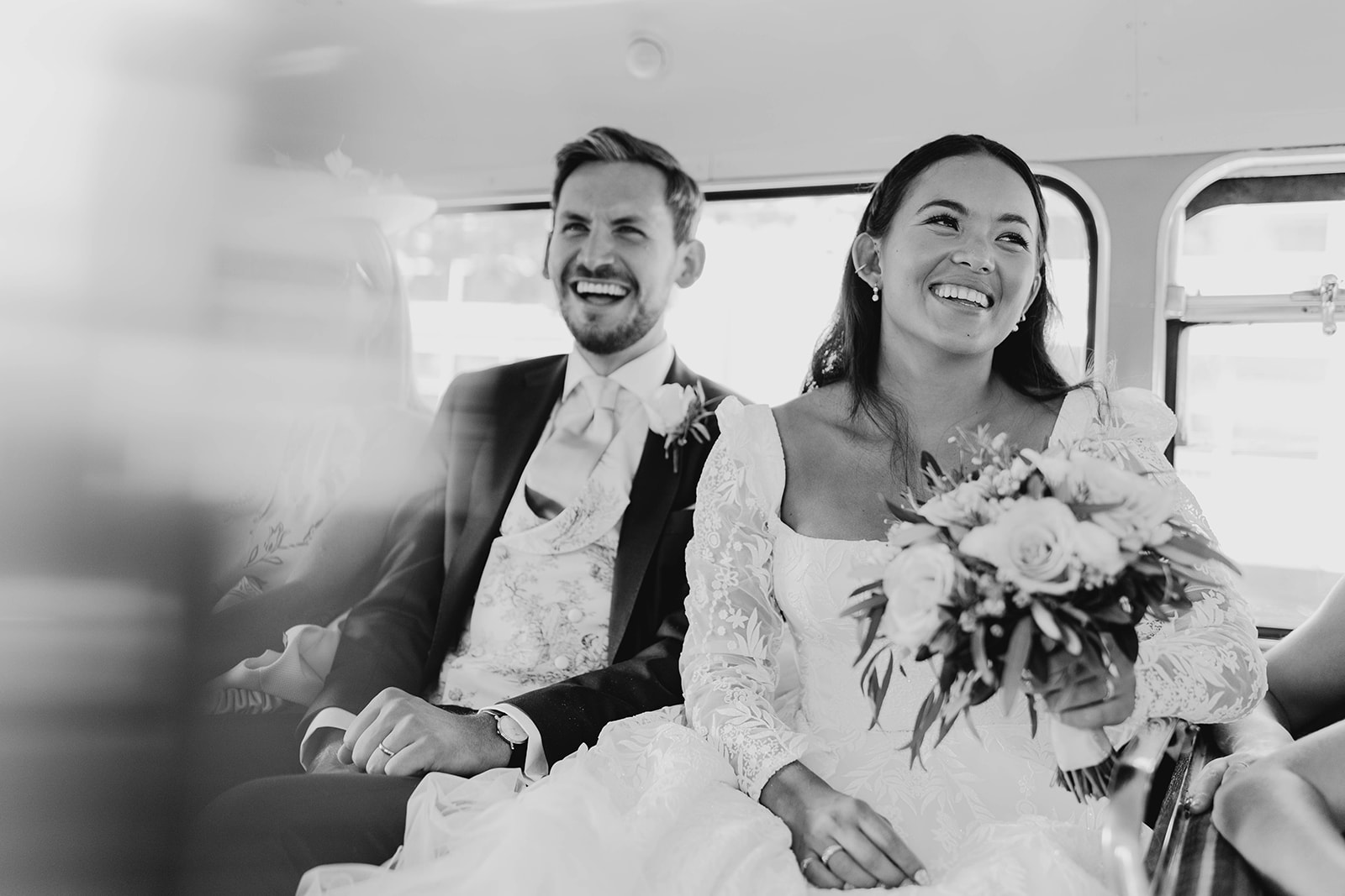 Bride and groom smiling as they get a red london bus to reception