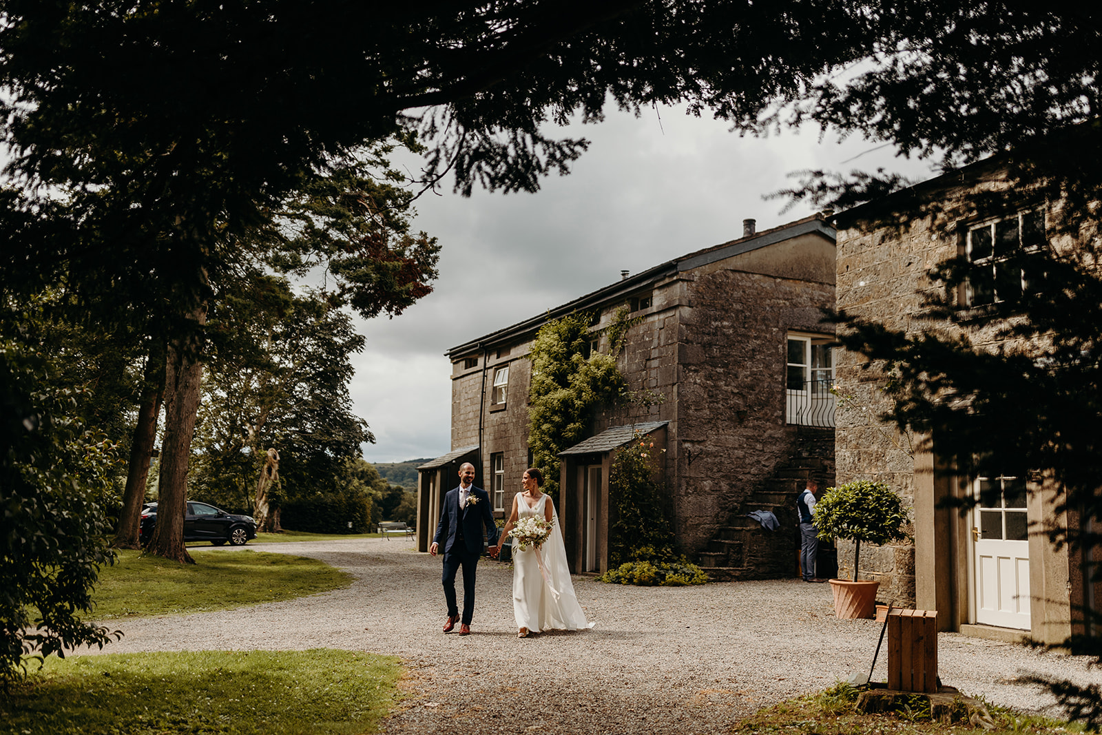 bride and groom walk with Longlands house in the background
