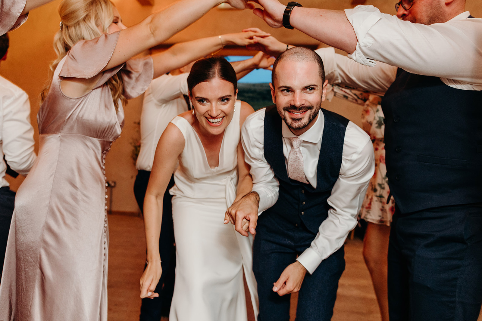Ceilidh dance at wedding, bride and groom go under guests arms