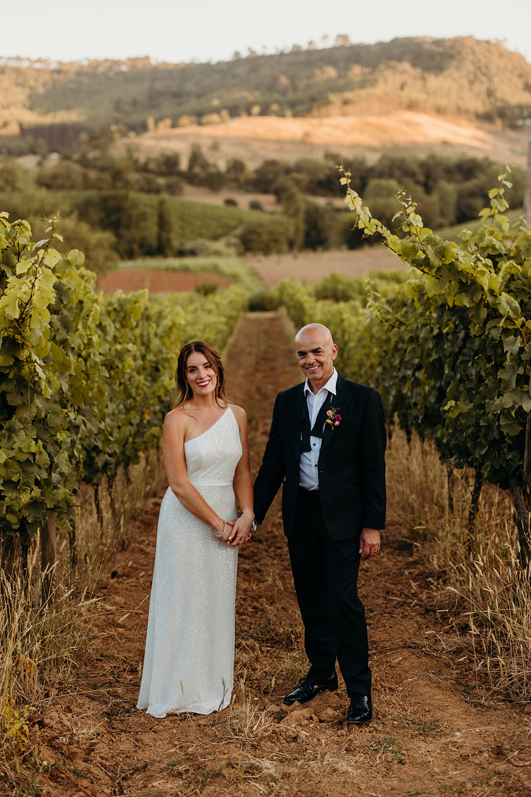 couple pose for photographs down winery vines