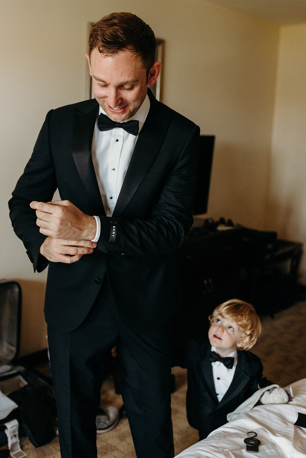Groom gets ready in black tie as son looks at him 