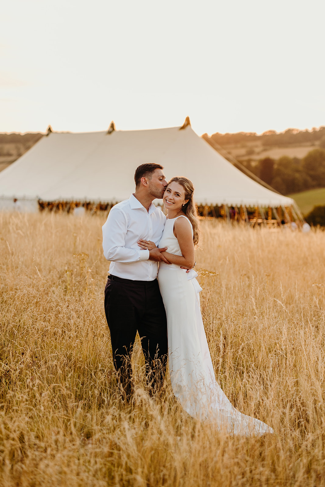 bride and groom pose at sunset with marquee in background 