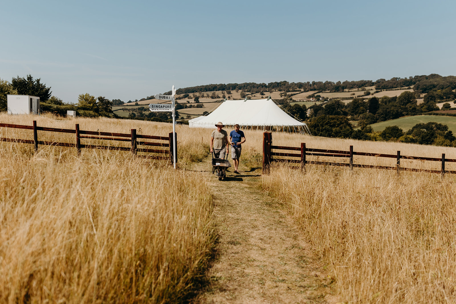 Tall sun burnt grass leading to white marquee for wedding 