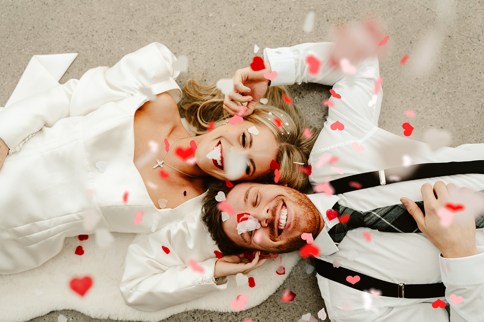 pink and red confetti falls on bride and groom photo taken from above as they lie on the floor