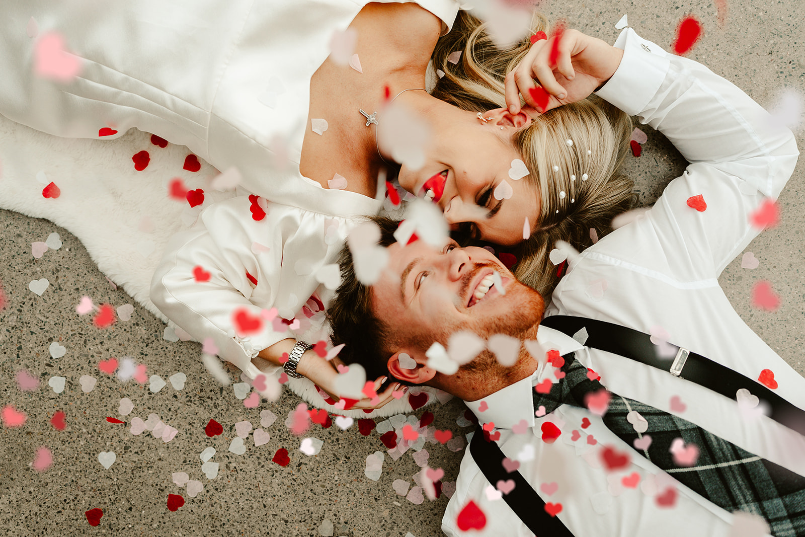 pink and red confetti falls on bride and groom photo taken from above as they lie on the floor