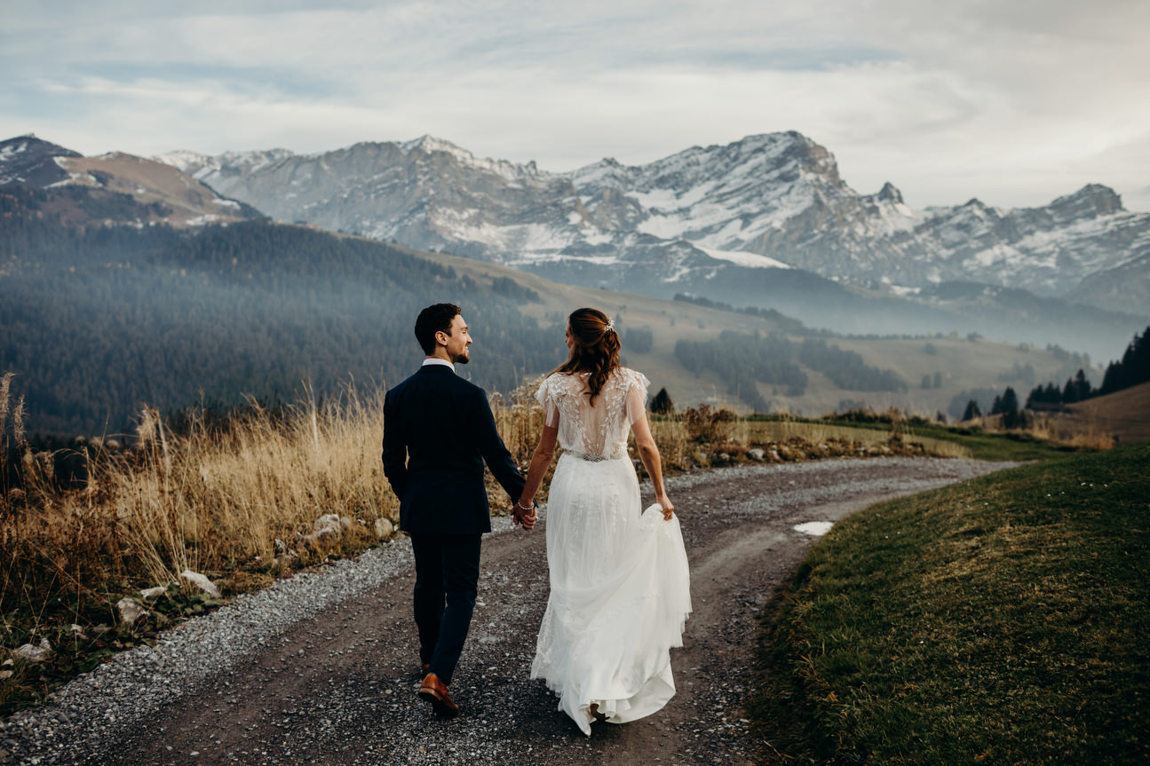 Bride and groom walk down gravel road with mountain view in background