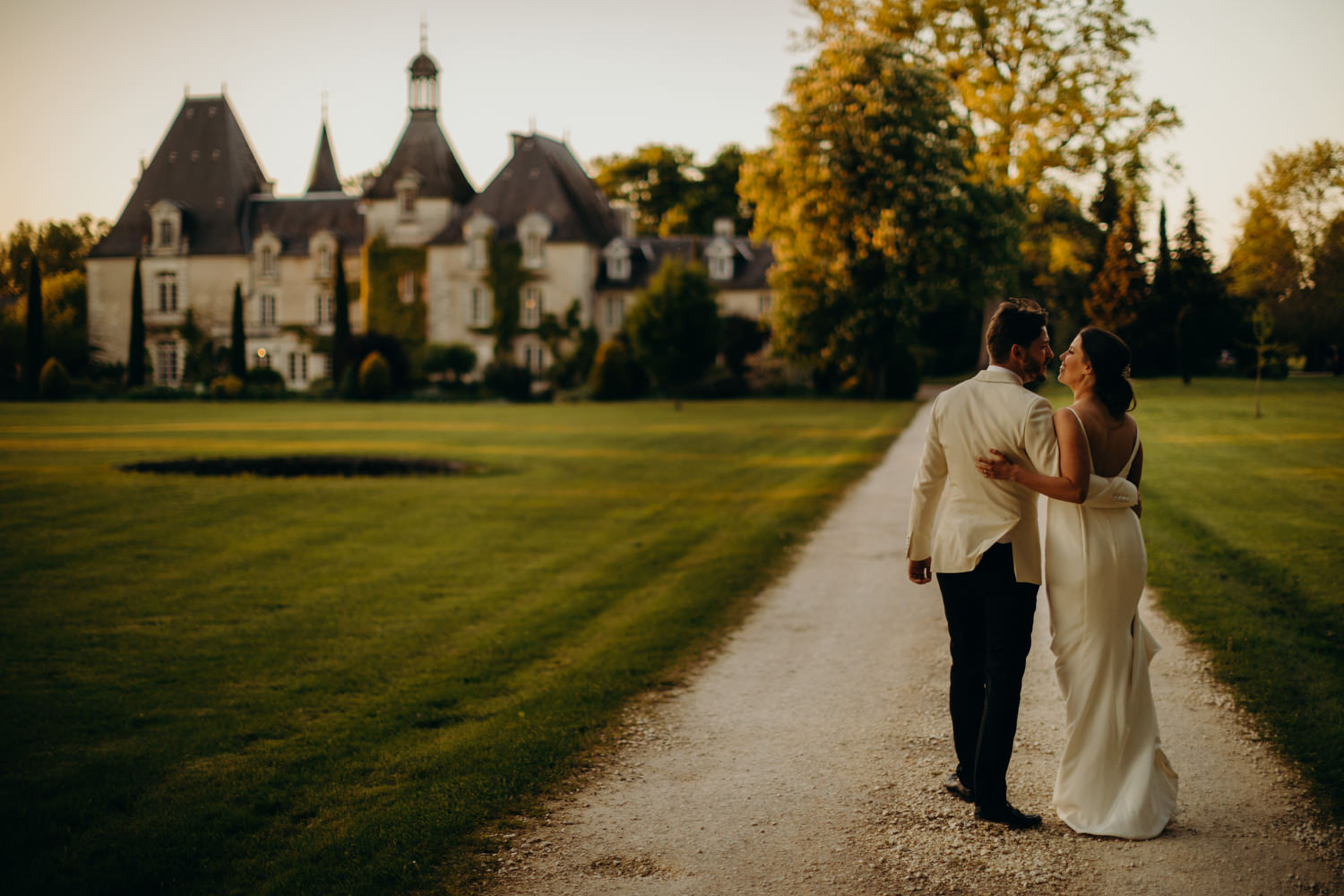 bride and groom walk down chateau driveway at sunset