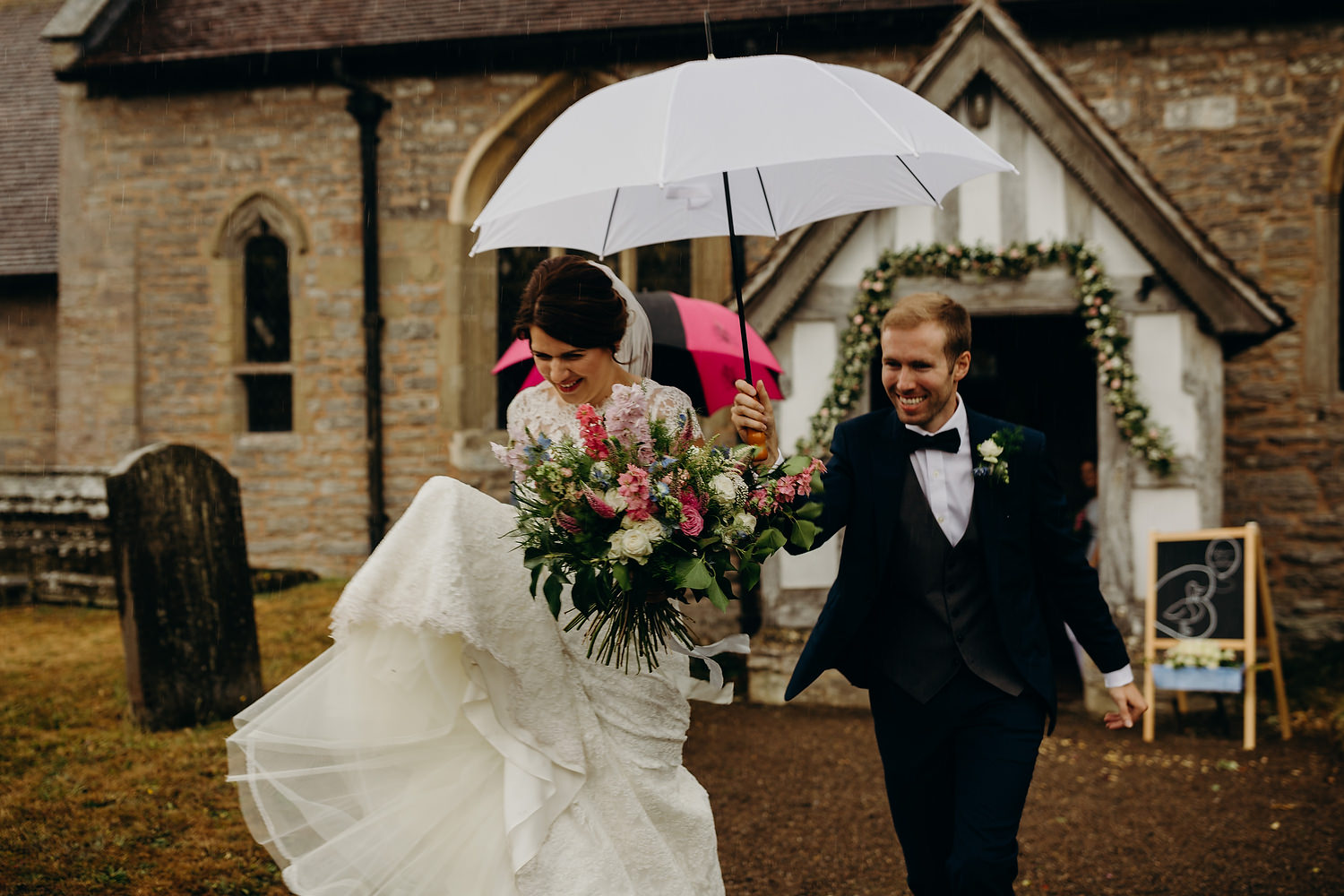 bride and groom running through rain after church ceremony