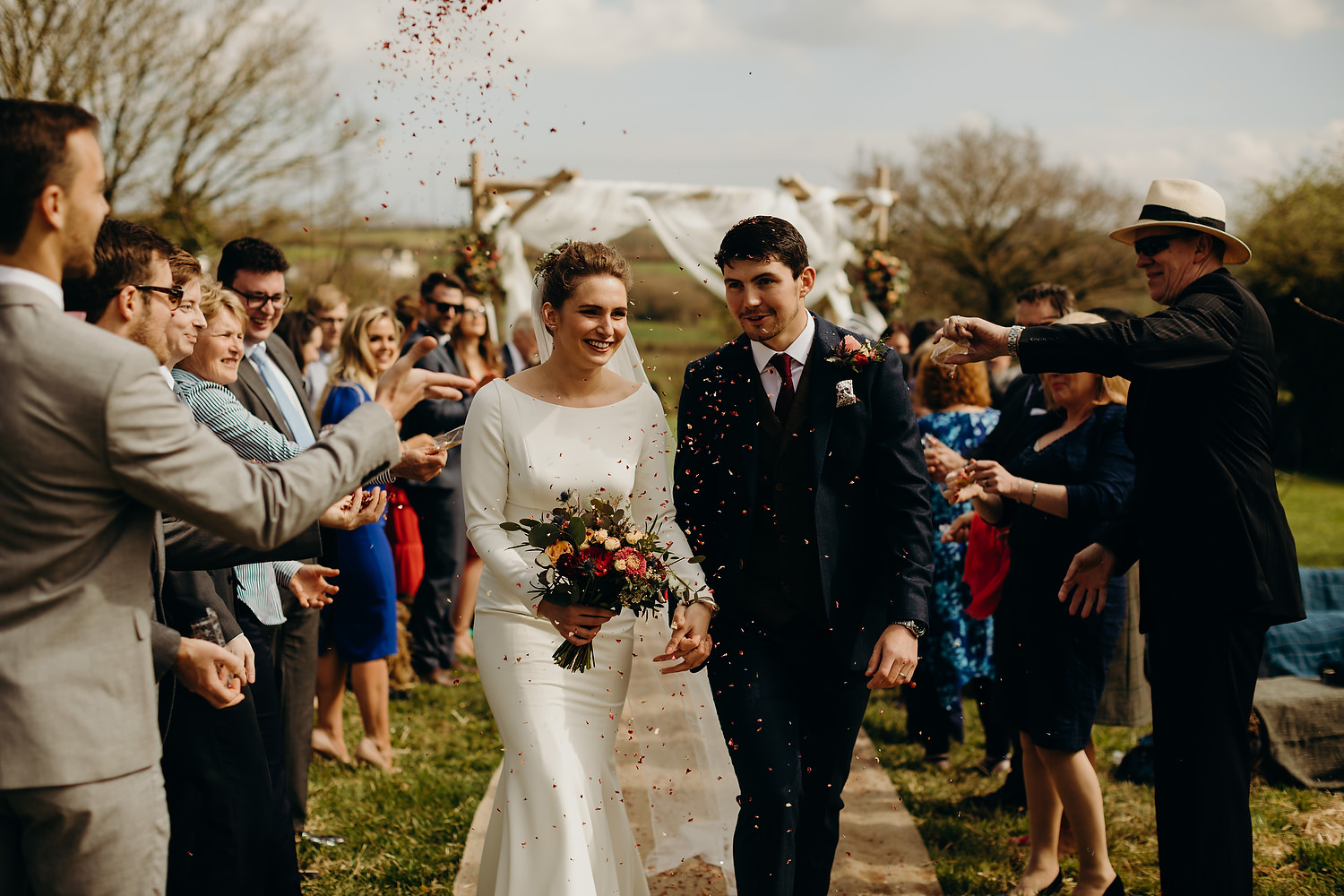 bride and groom confetti photograph as they walk down outdoor aisle