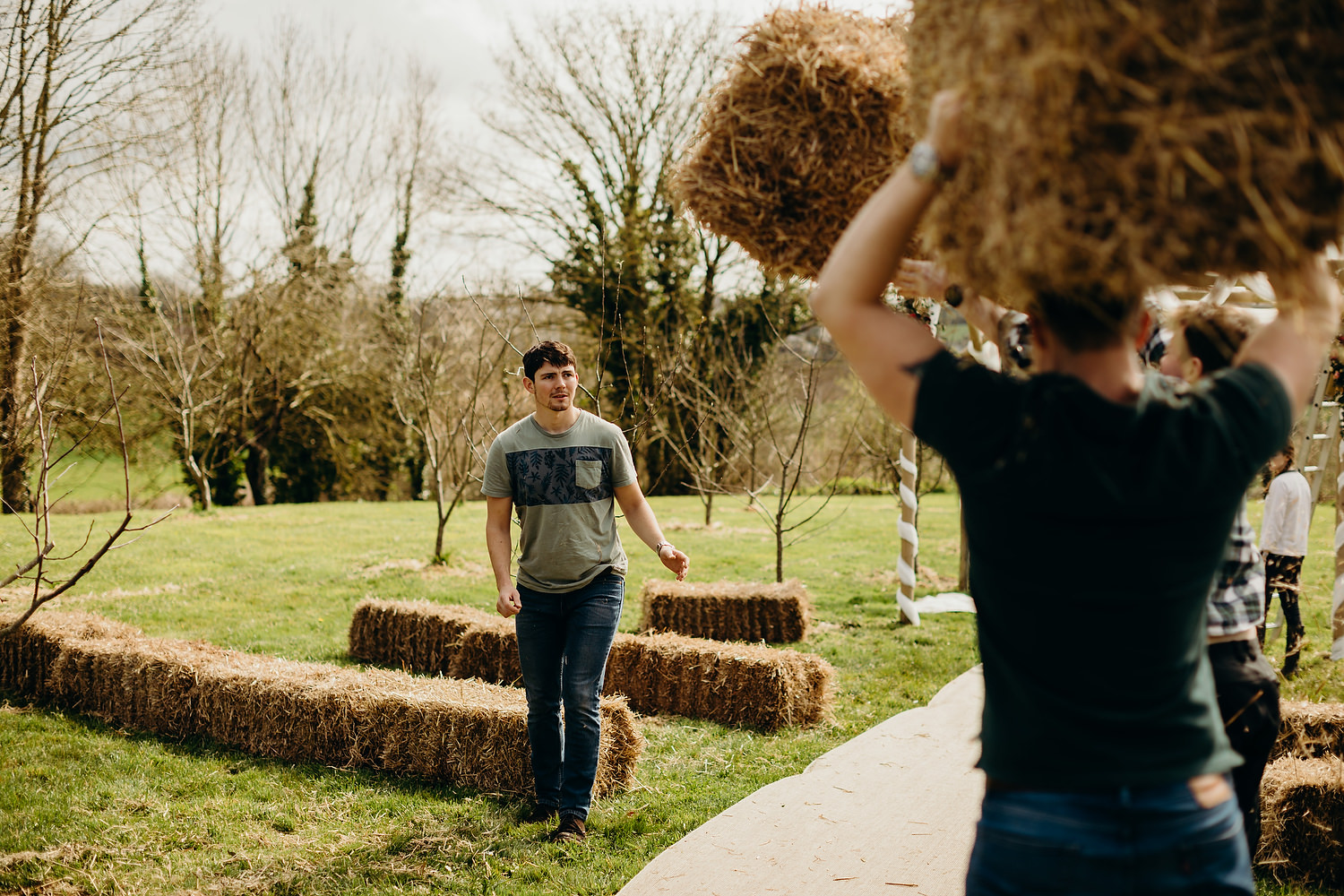 groom helping put out hay stacks for outdoor wedding