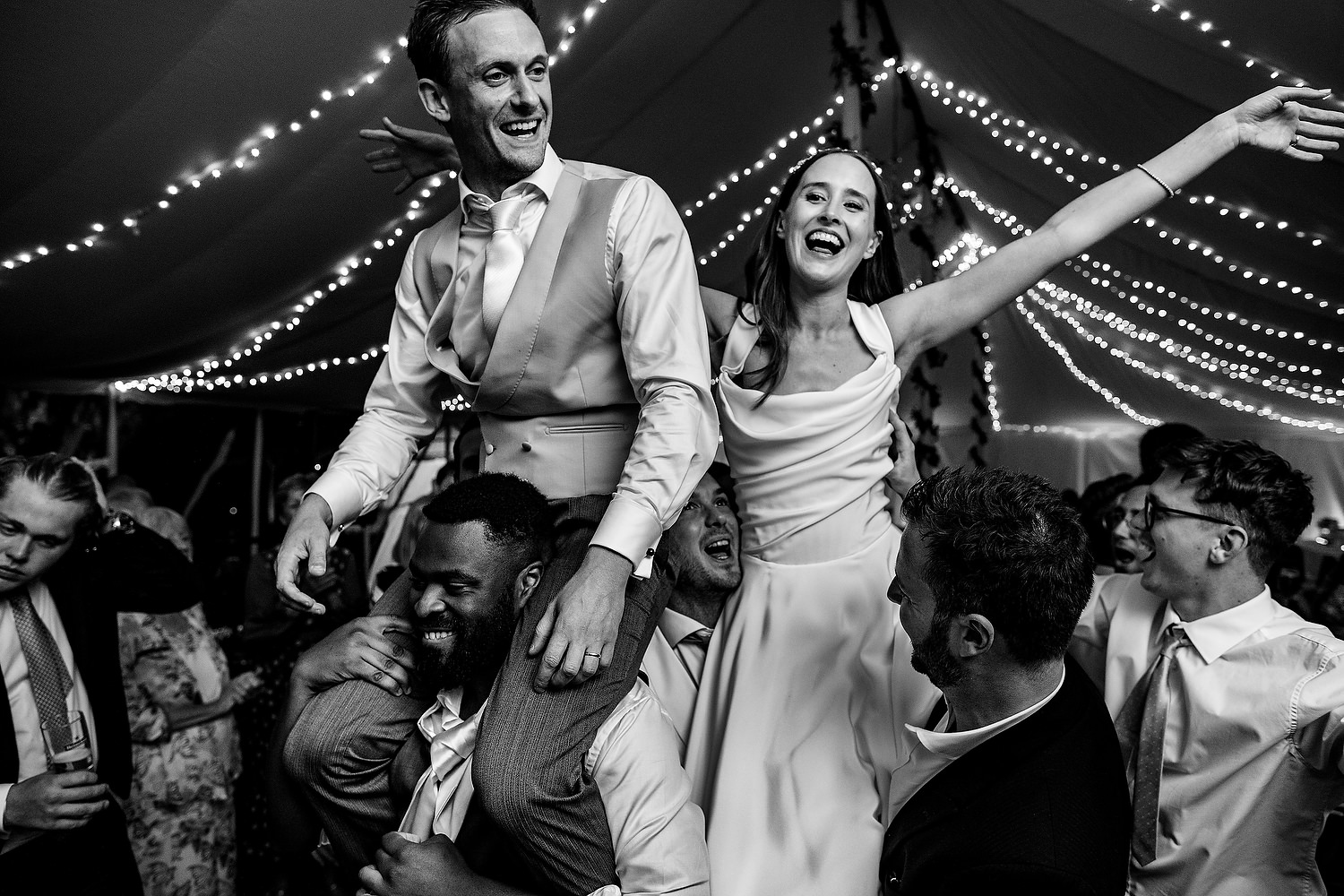 bride and groom on shoulders during wedding party