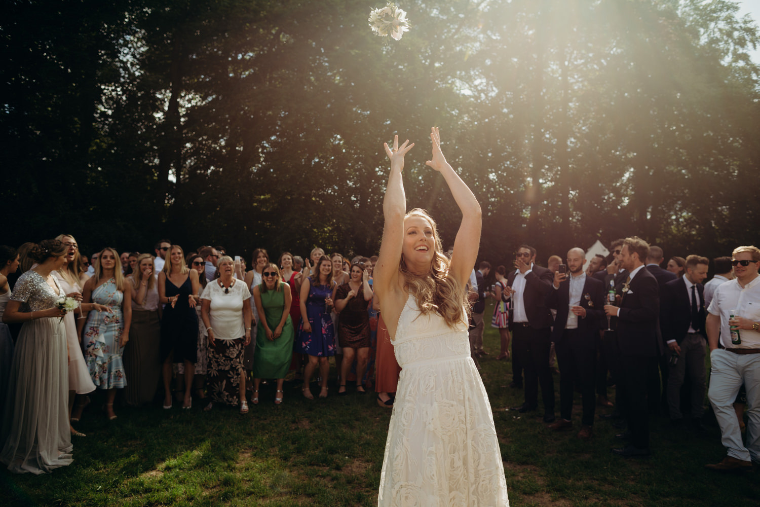 bride throwing bouquet up in the air as guests prepare to catch