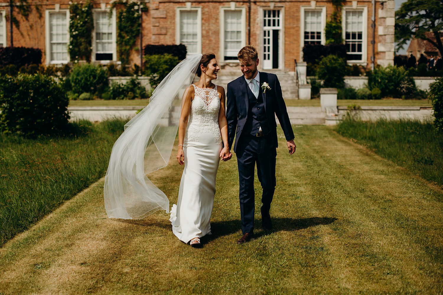 bride and groom walking on lawn with country house in background