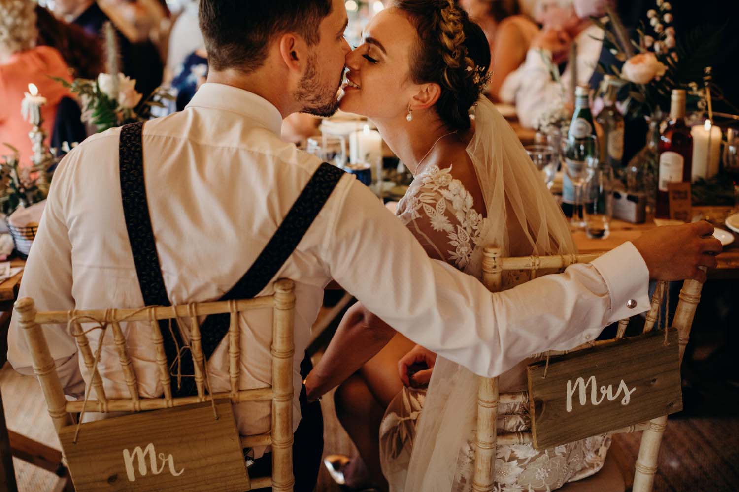bride and groom kiss at dinner table with name tags hanging from chairs
