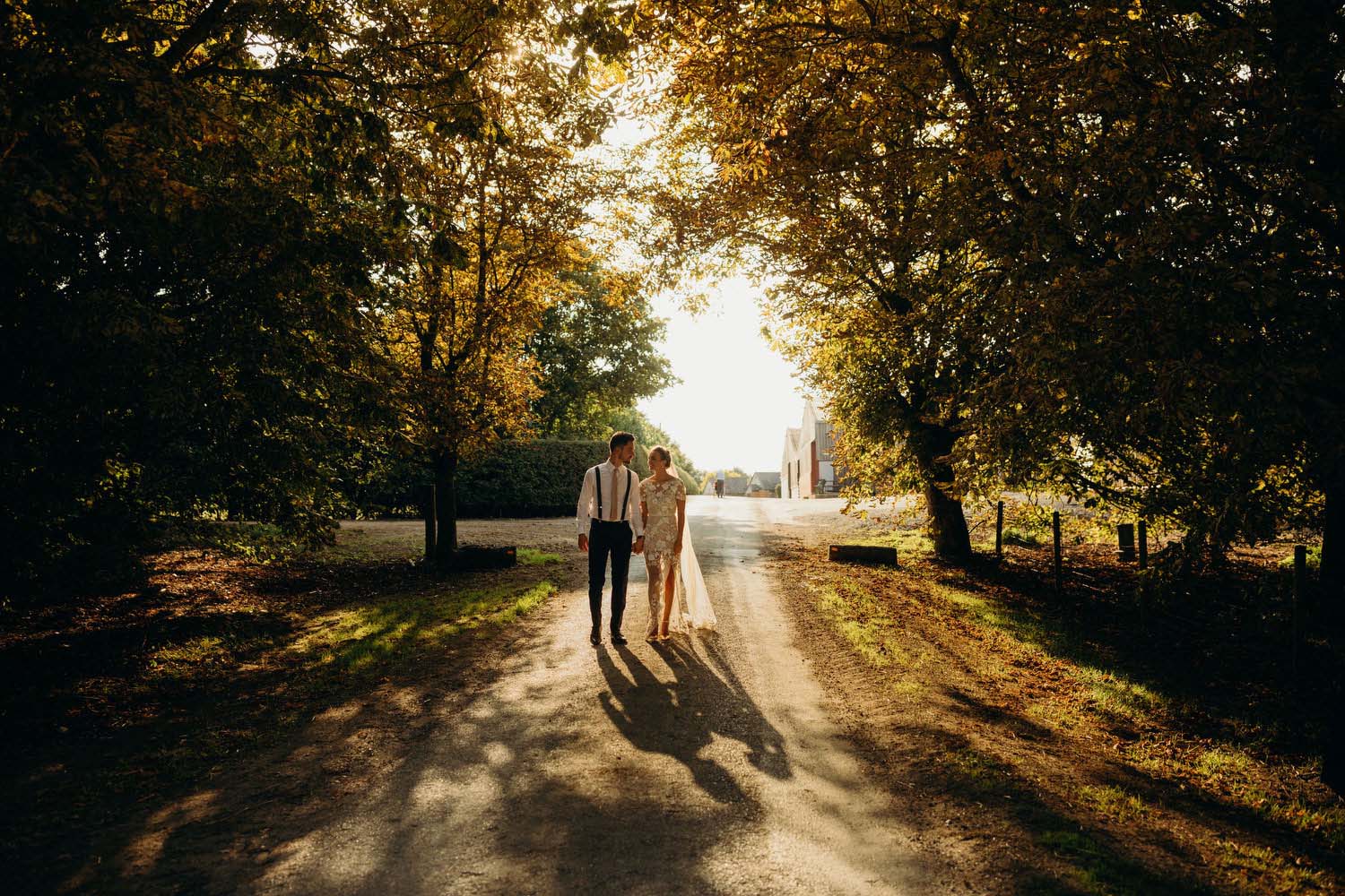 Bride and groom walk at sunset on wooded driveway at Buckinghamshrire wedding