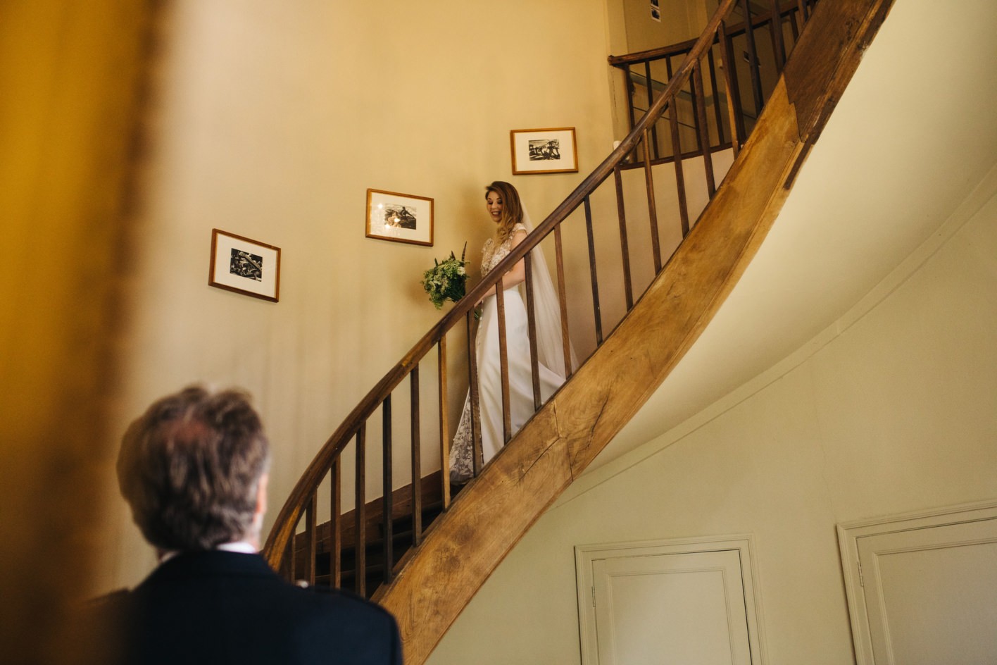 bride walks down stairs with dad waiting at bottom 