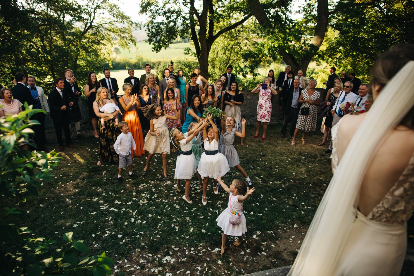 Flower girls try and catch bouquet thrown by bride on lawn of chateau 
