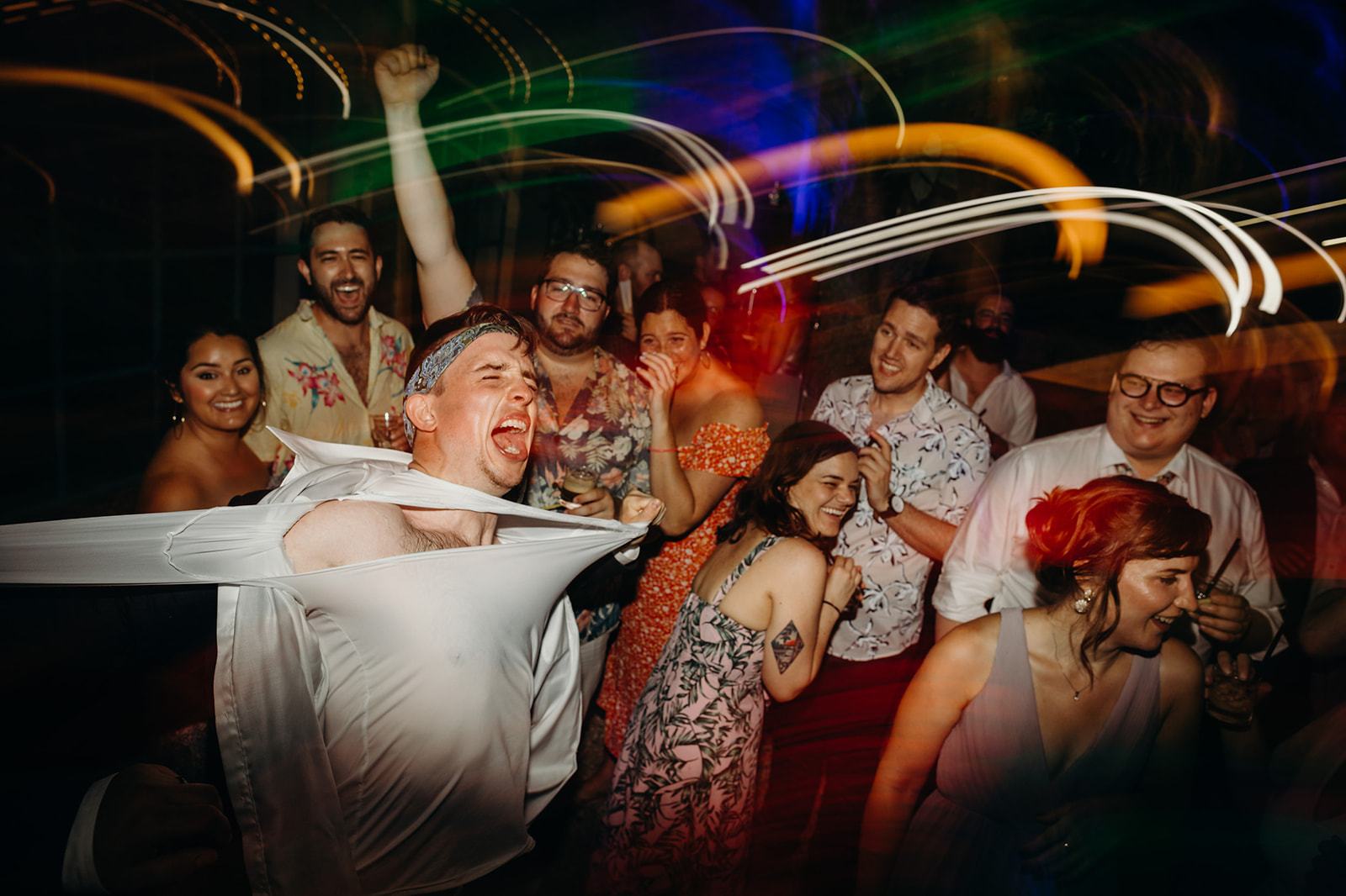 Documentary wedding photograph of joyful people dancing at a party with colourful light streaks in the background.