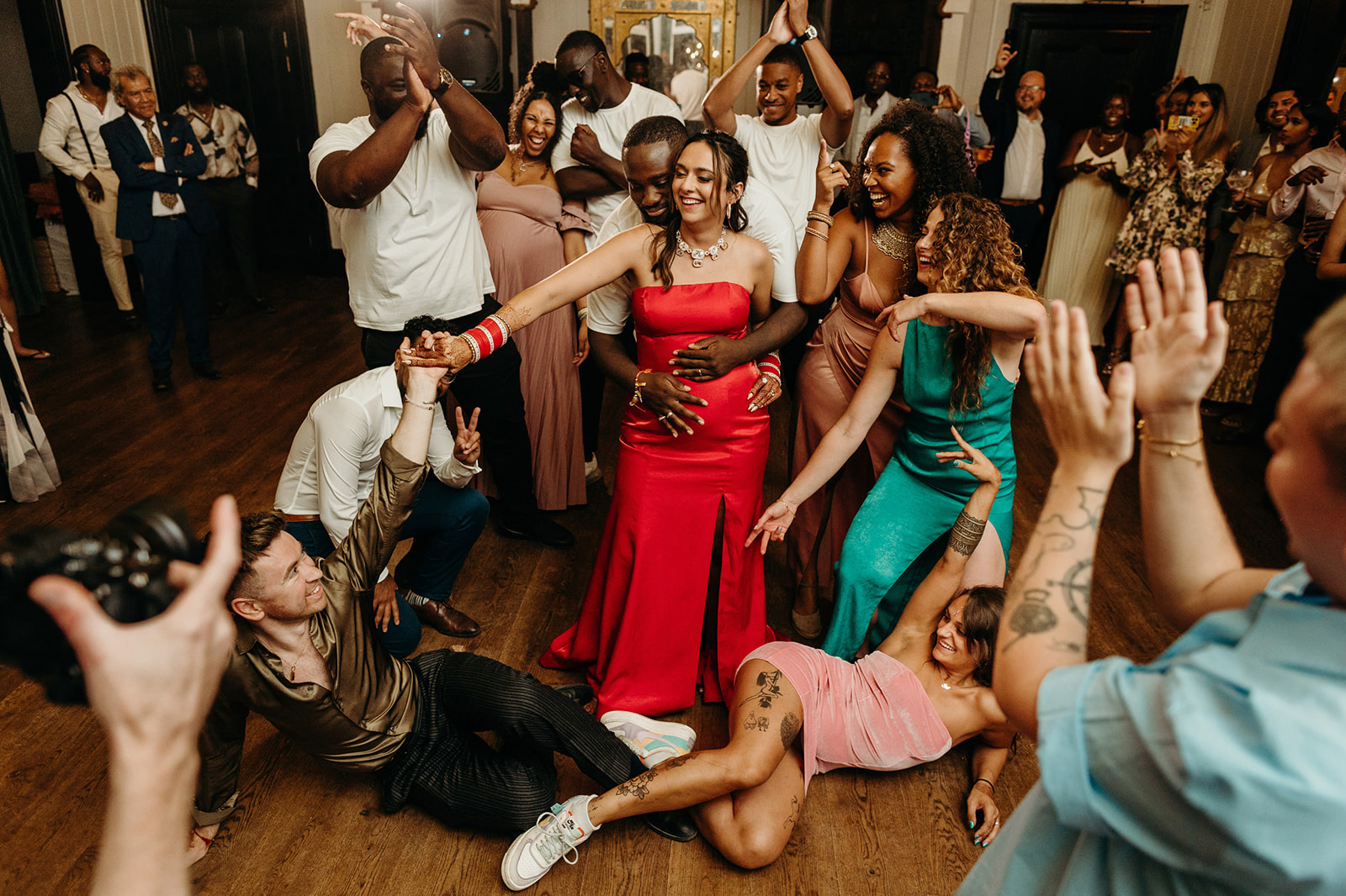 Unobtrusive shot of an exuberant group dancing at a party, highlighting a woman in a red dress with a radiant smile.