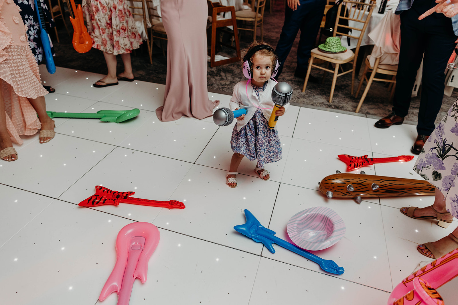Documentary wedding photography captures a young girl with a toy microphone, standing amidst inflatable guitars 