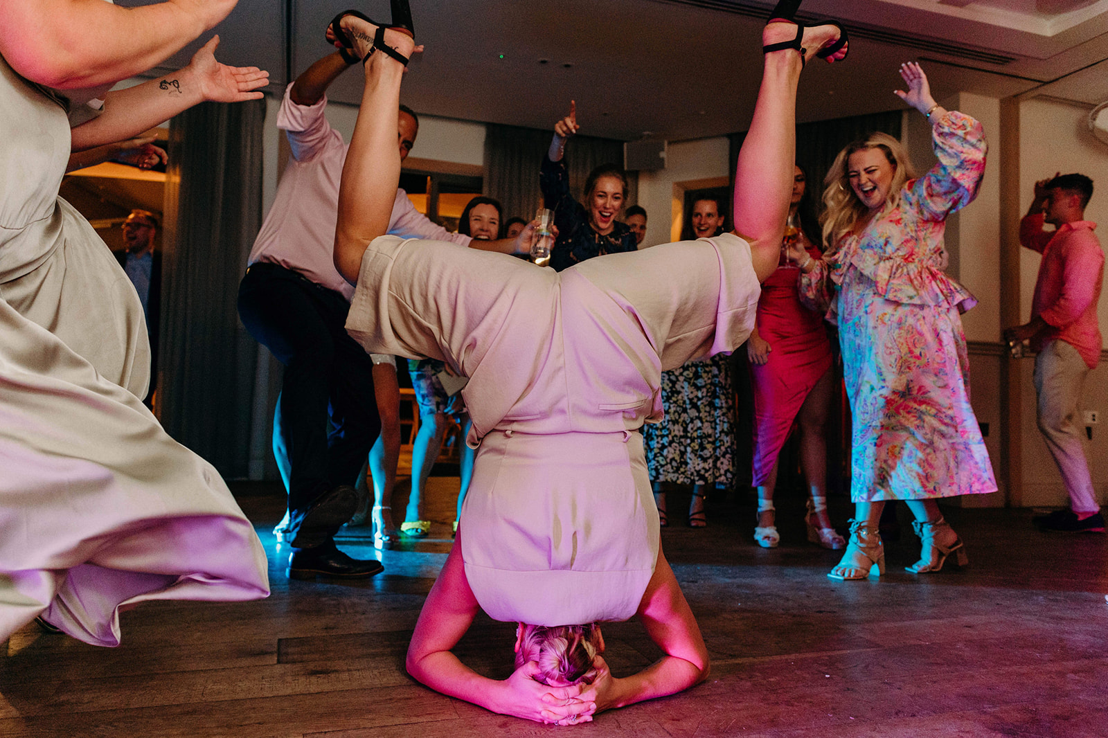 Energetic wedding moment: Guest performs a headstand on the dance floor, surrounded by cheering crowd at a lively party.