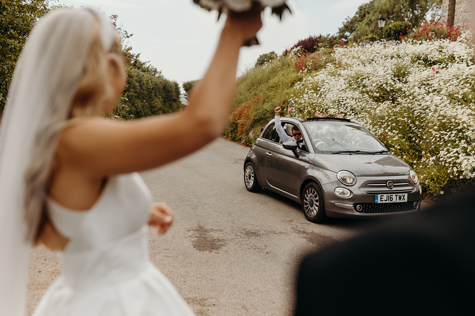Unobtrusive shot of a bride acknowledging friends in a passing vehicle after her church wedding