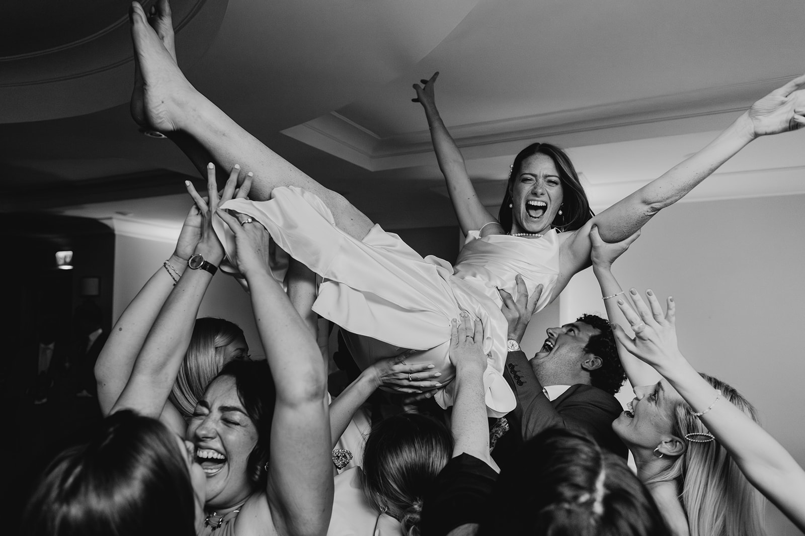 Documentary style wedding image depicts a happy bride being lifted by guests, all smiling and celebrating at a joyous re