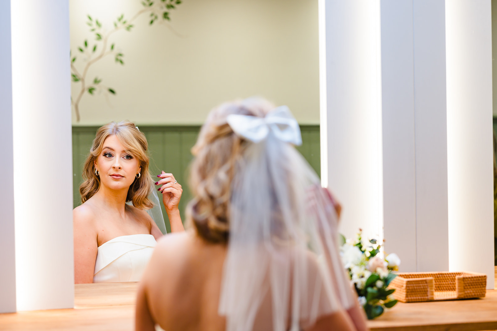 bride getting ready and looking in mirror with white bow and veil on