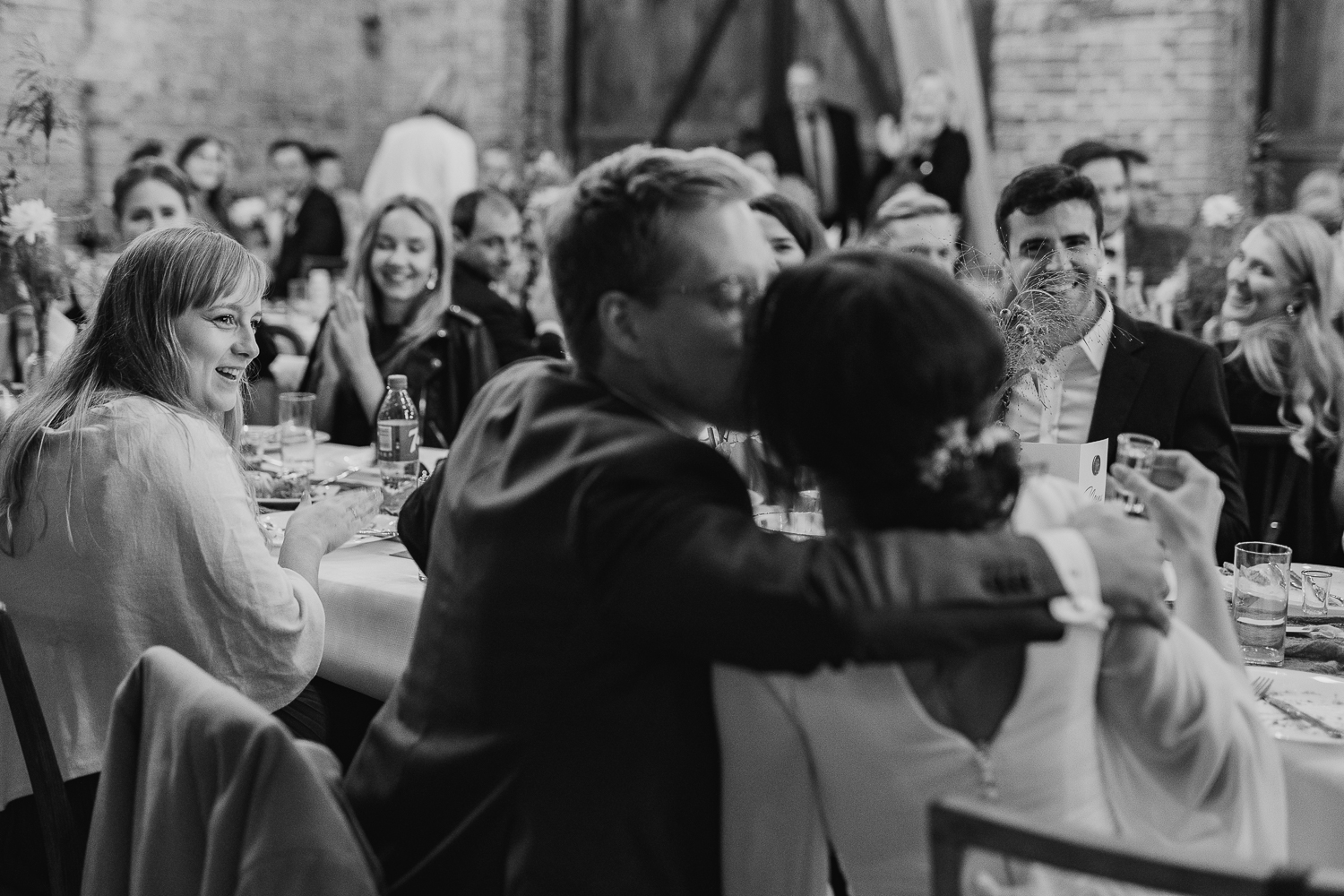 Kadr z fotoreportażu ślubnego, przedstawiający pocałunek pary młodej przy stole weselnym.
