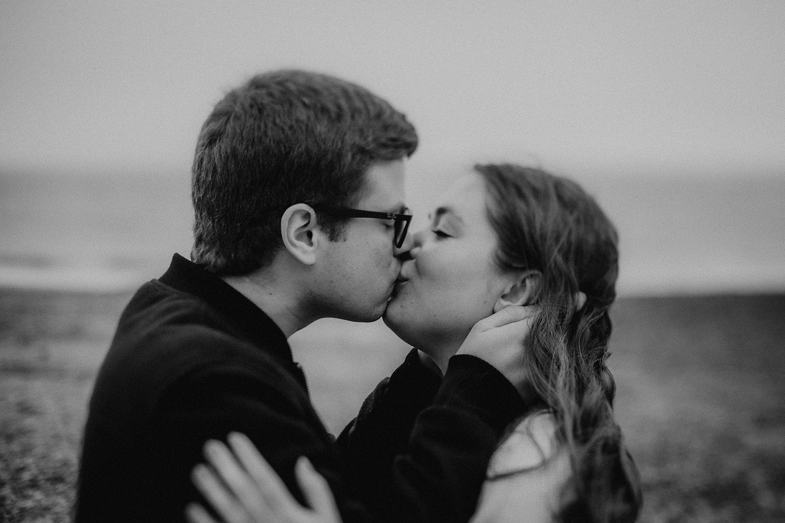 Black and white photo of a couple kissing in front of the sea on their Highcliffe Beach engagement photoshoot. 