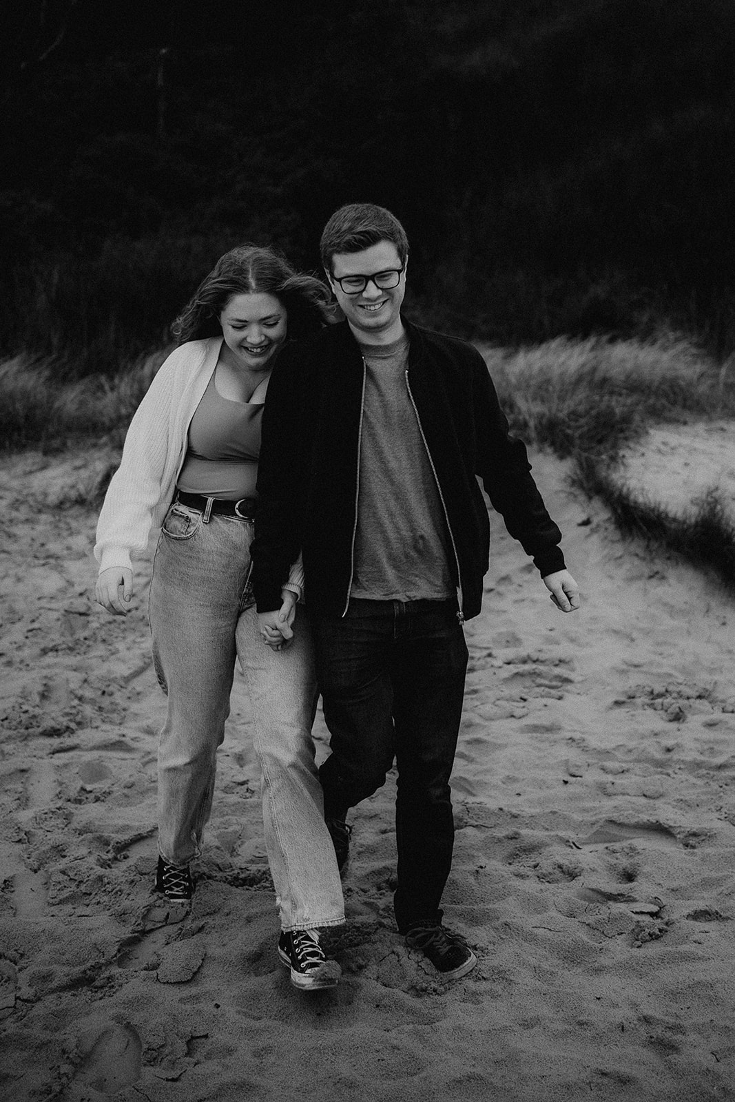 Black and white photo of couple running on sand dunes hand in hand at their pre-wedding photoshoot on Highcliffe Beach