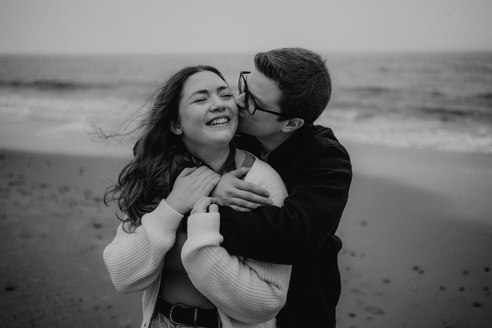 black and white photo of couple snuggling in front of the sea on their Highcliffe beach pre-wedding photoshoot