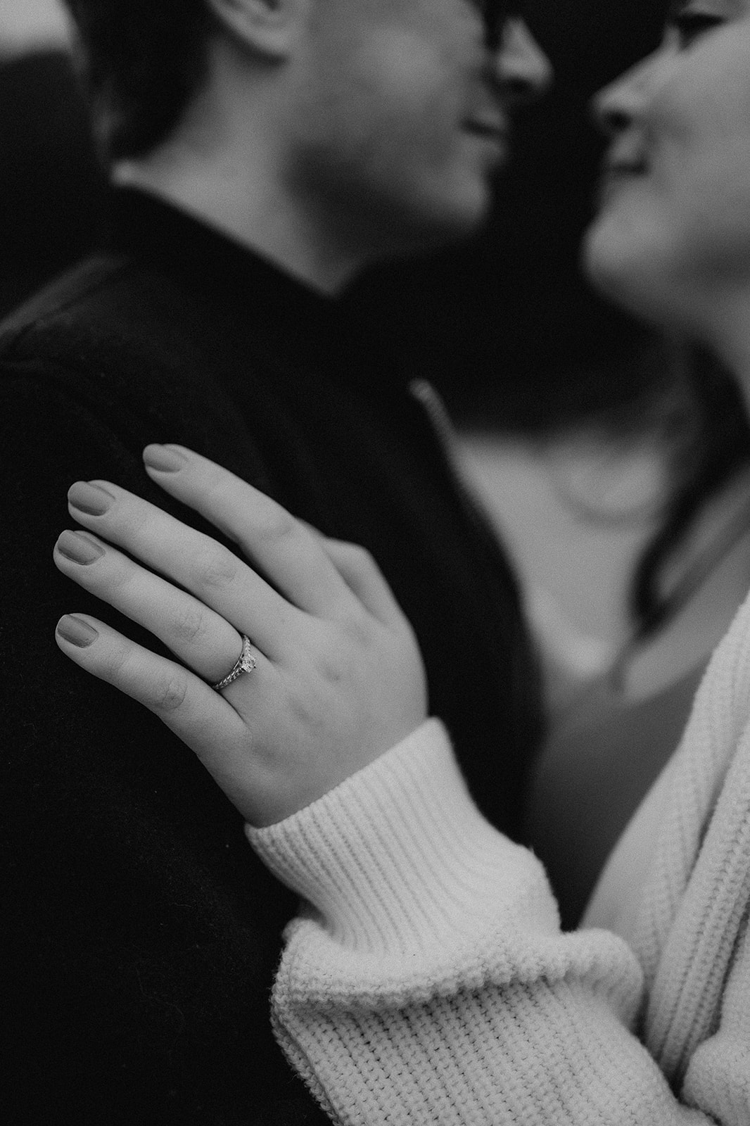 Black and white photo of a woman's engagement ring on her fiance's arm at their pre-wedding photoshoot at Highcliffe