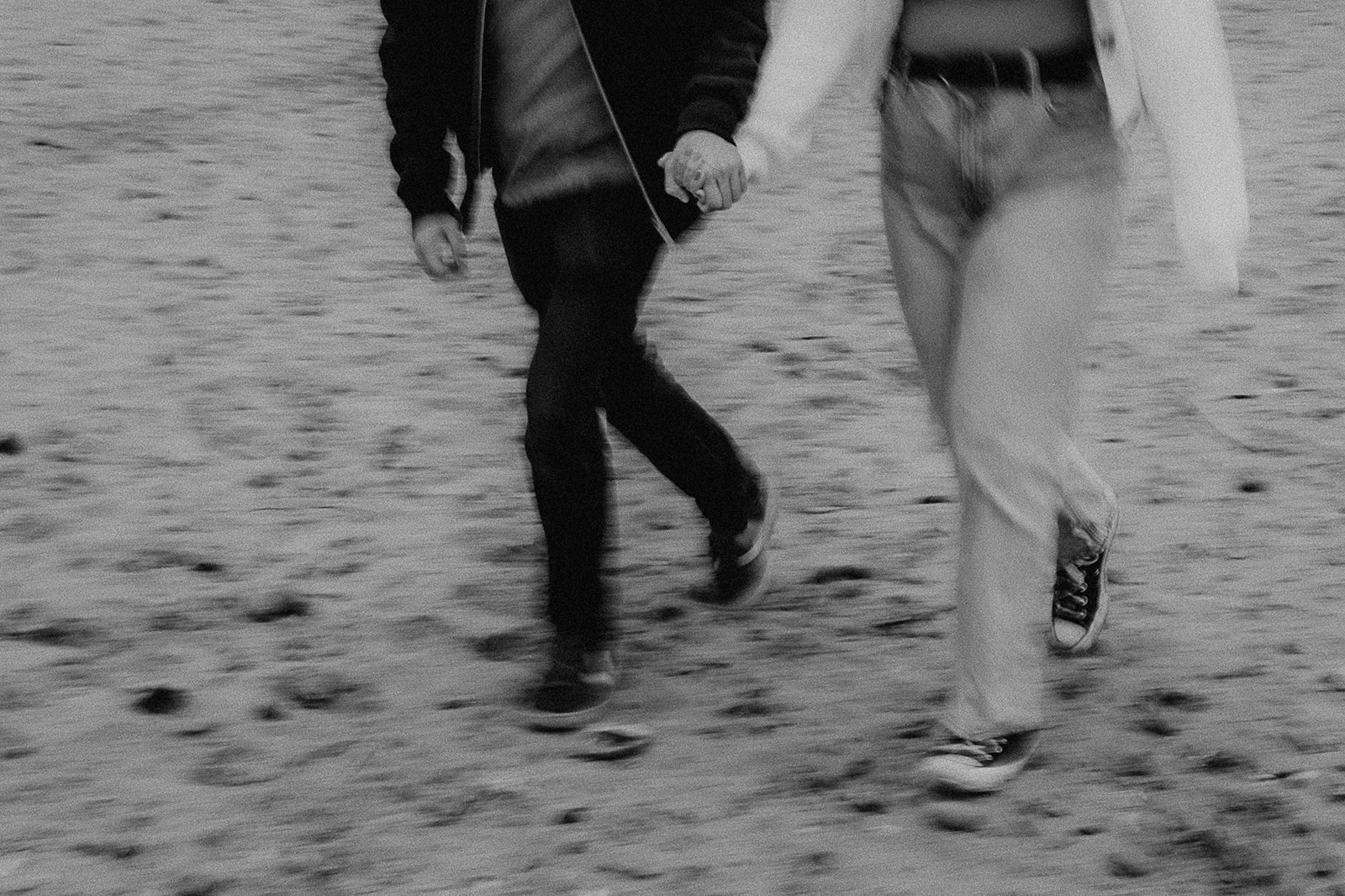 Blurry image of a couple running along the beach, only their legs and holding hands are visible. 