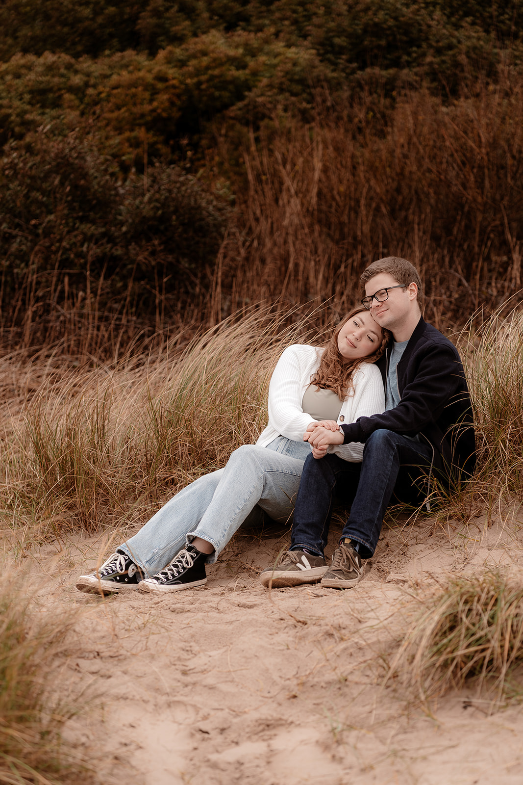 Couple cuddle together in the sand dunes on Highcliffe Beach for their pre-wedding photoshoot. 