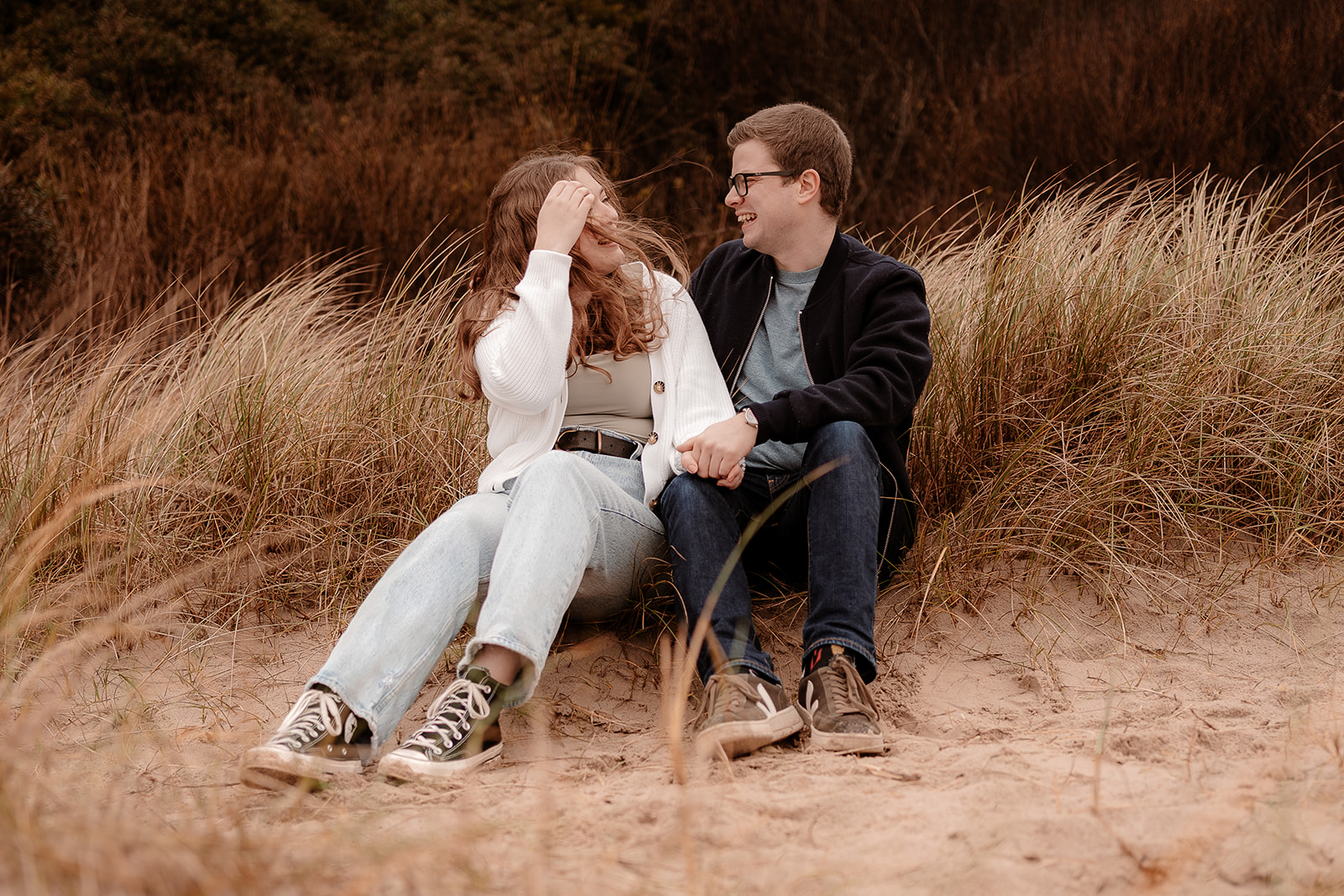 A couple sit together on the sand dunes at Highcliffe Beach at their pre-wedding photoshoot. 