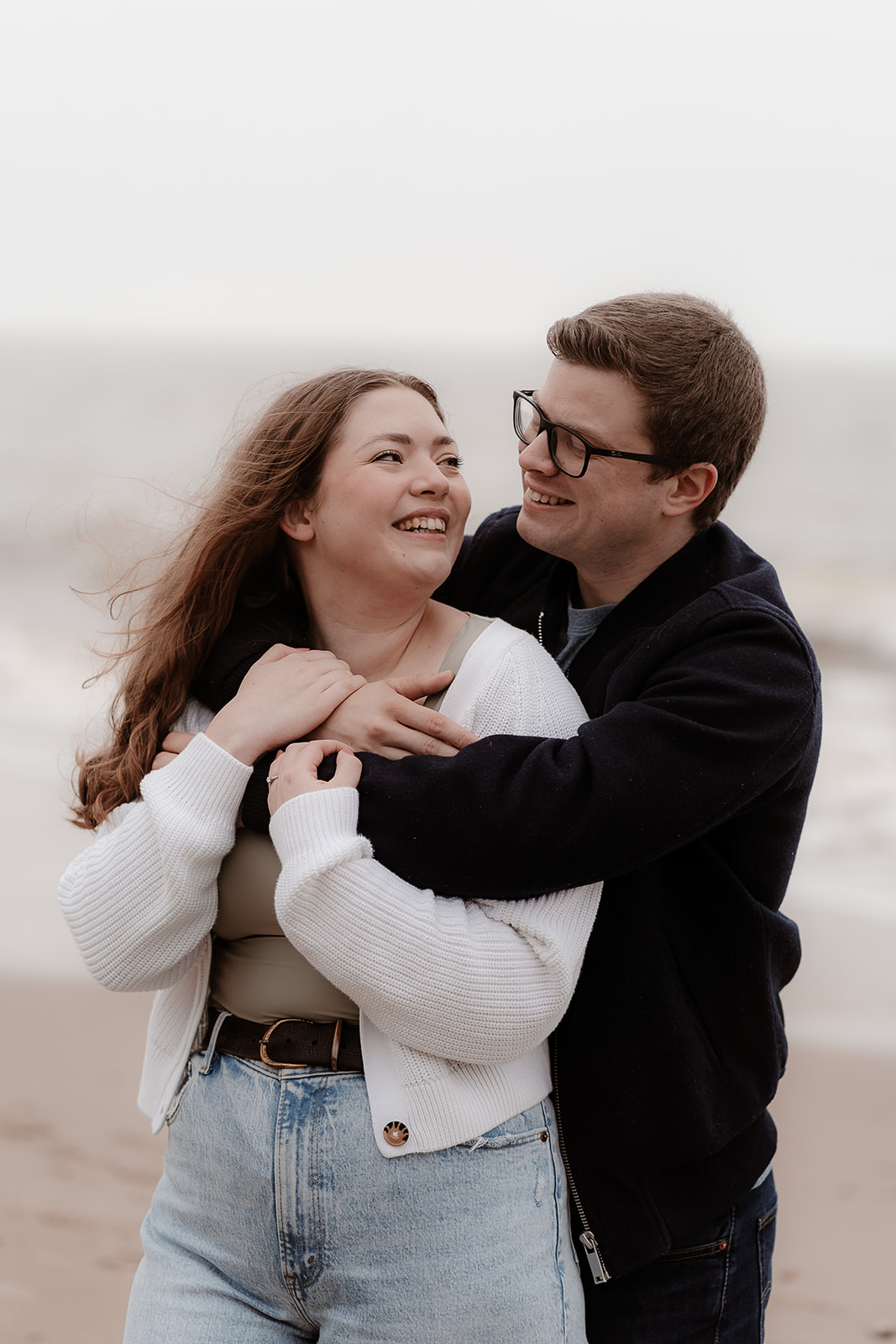 Couple snuggle on the beach with the sea behind them on their Highcliffe beach engagement photoshoot