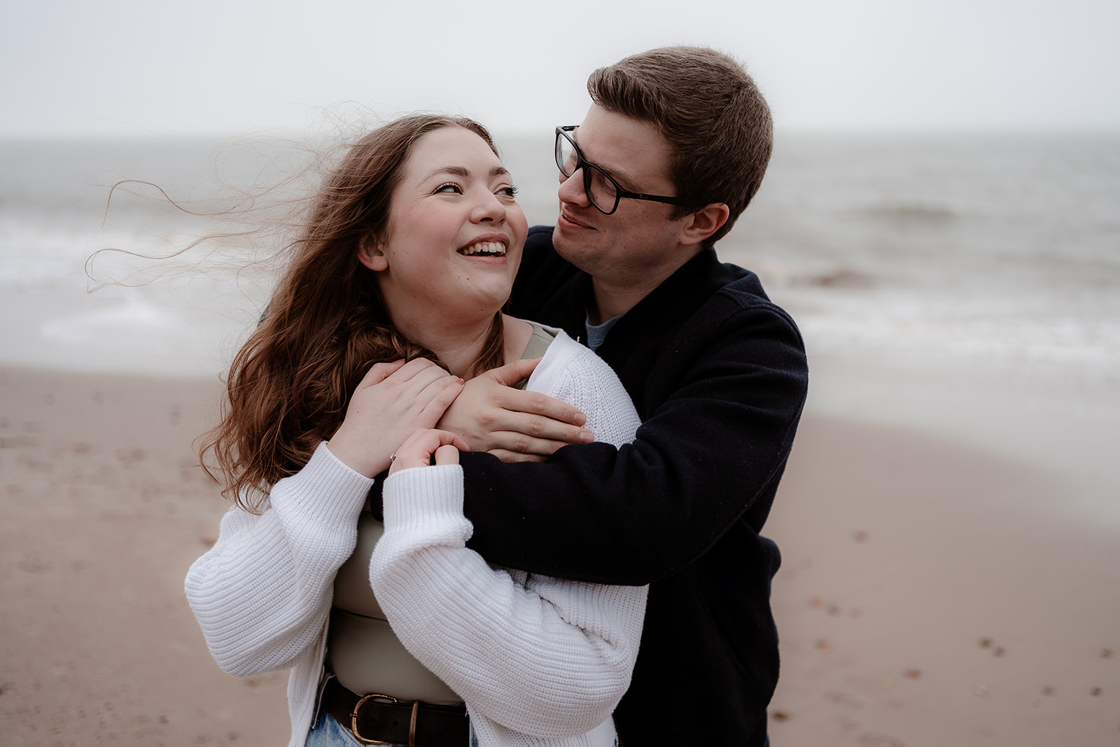 Couple snuggle on the beach with the sea behind them on their Highcliffe beach pre-wedding photoshoot