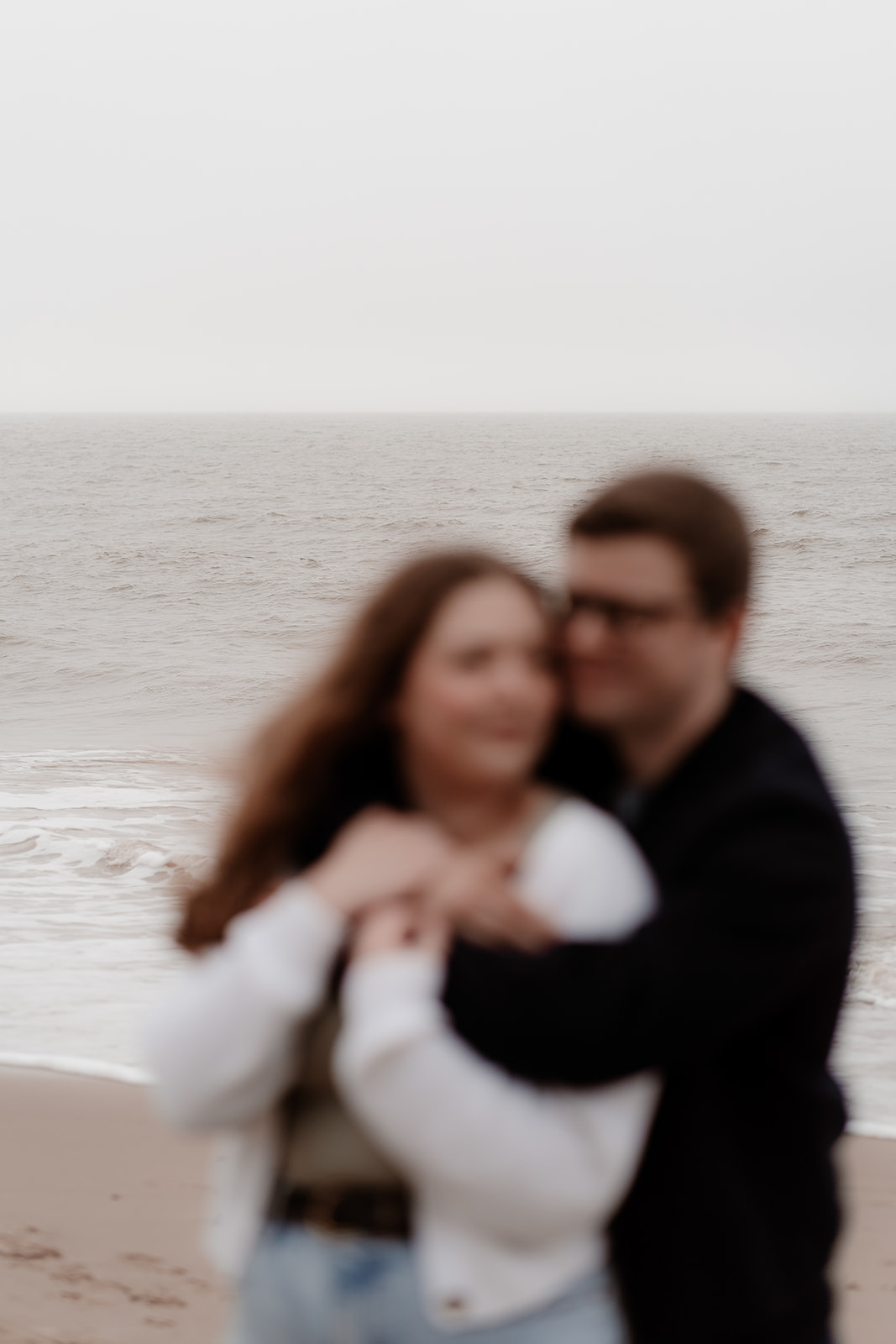 Couple in the foreground are blurry, with the focus on the sea in the background - Highcliffe beach engagement shoot