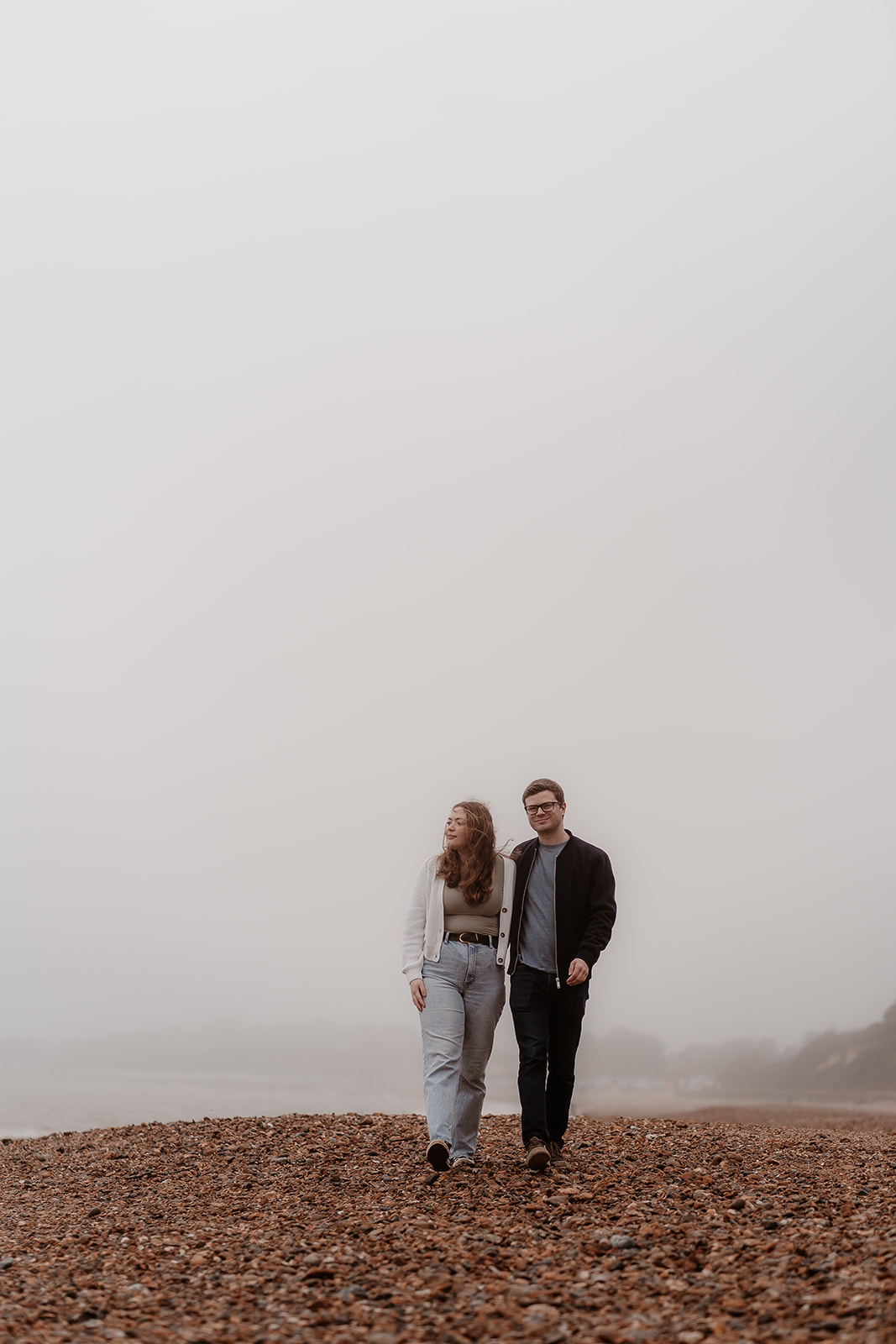Couple walk along the misty, moody beach at their Highcliffe engagement shoot
