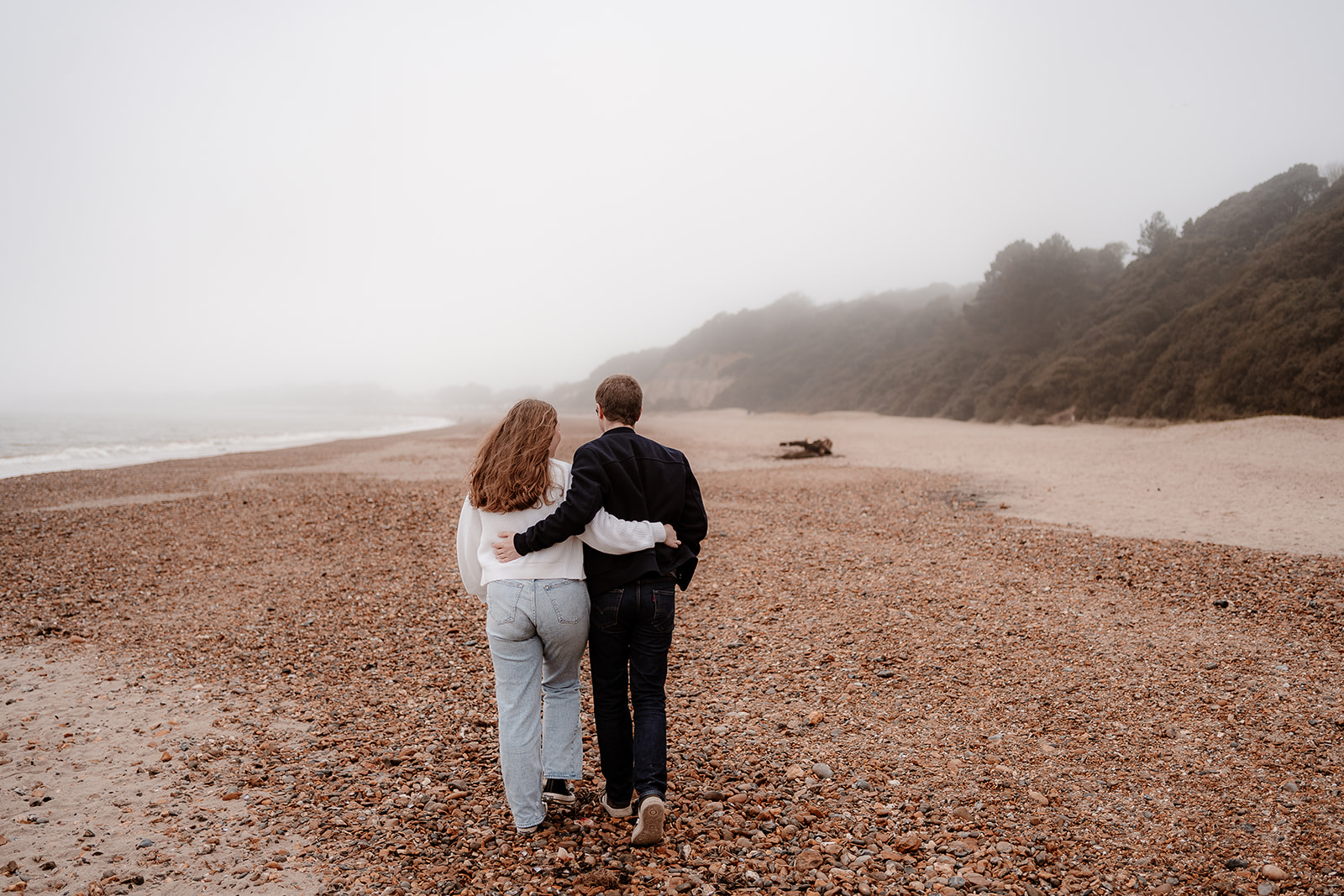 Couple walk away along Highcliffe Beach with their arms around each other