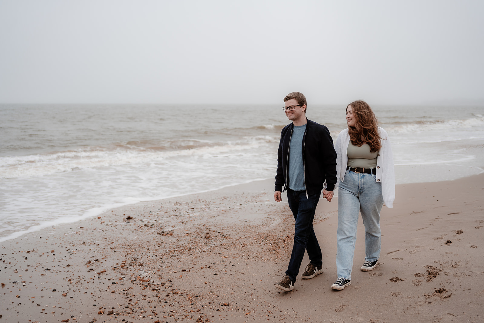 Couple walk hand in hand along Highcliffe Beach for their pre-wedding photoshoot. 