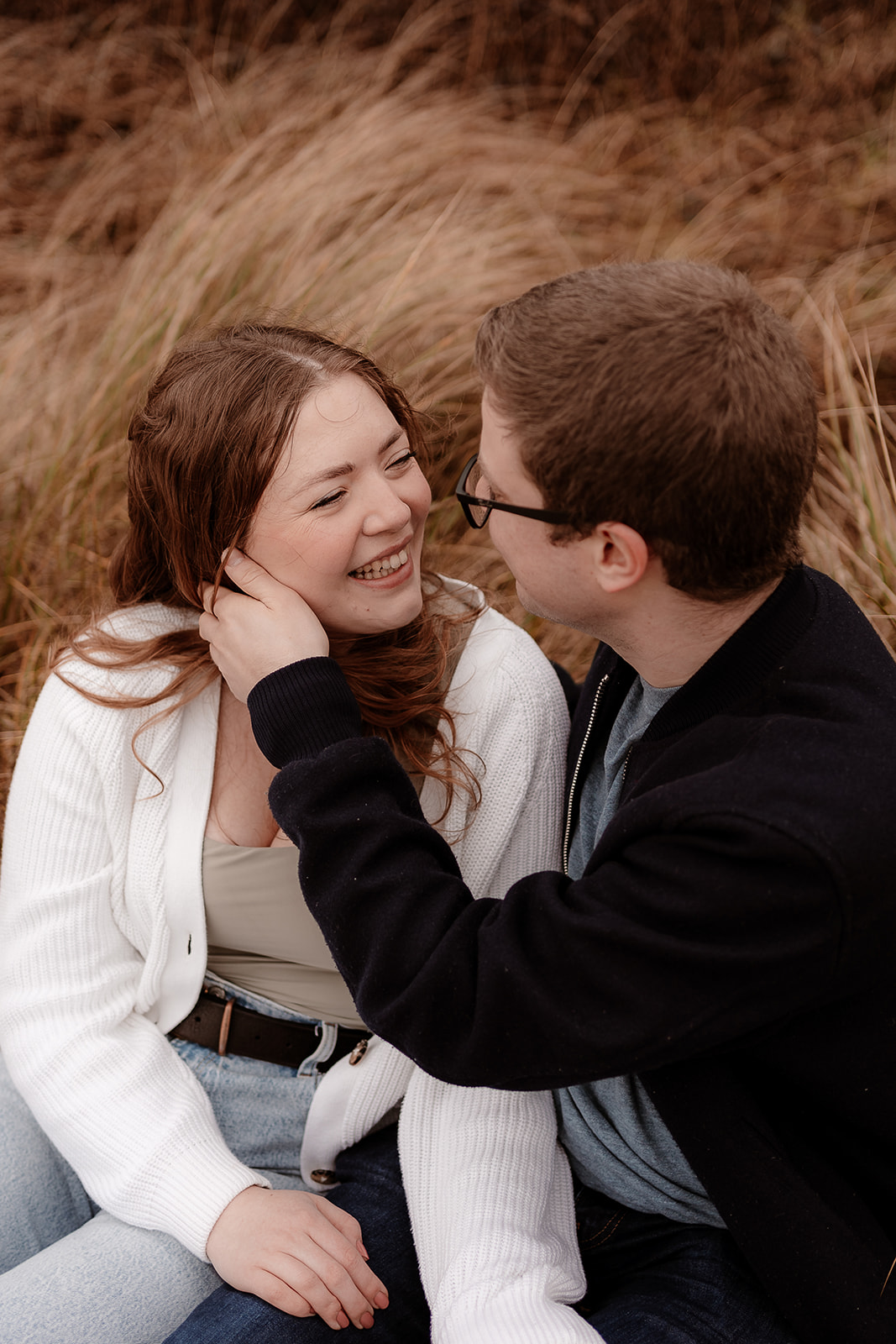 A man strokes the hair out of his fiance's face on their Highcliffe Beach engagement shoot