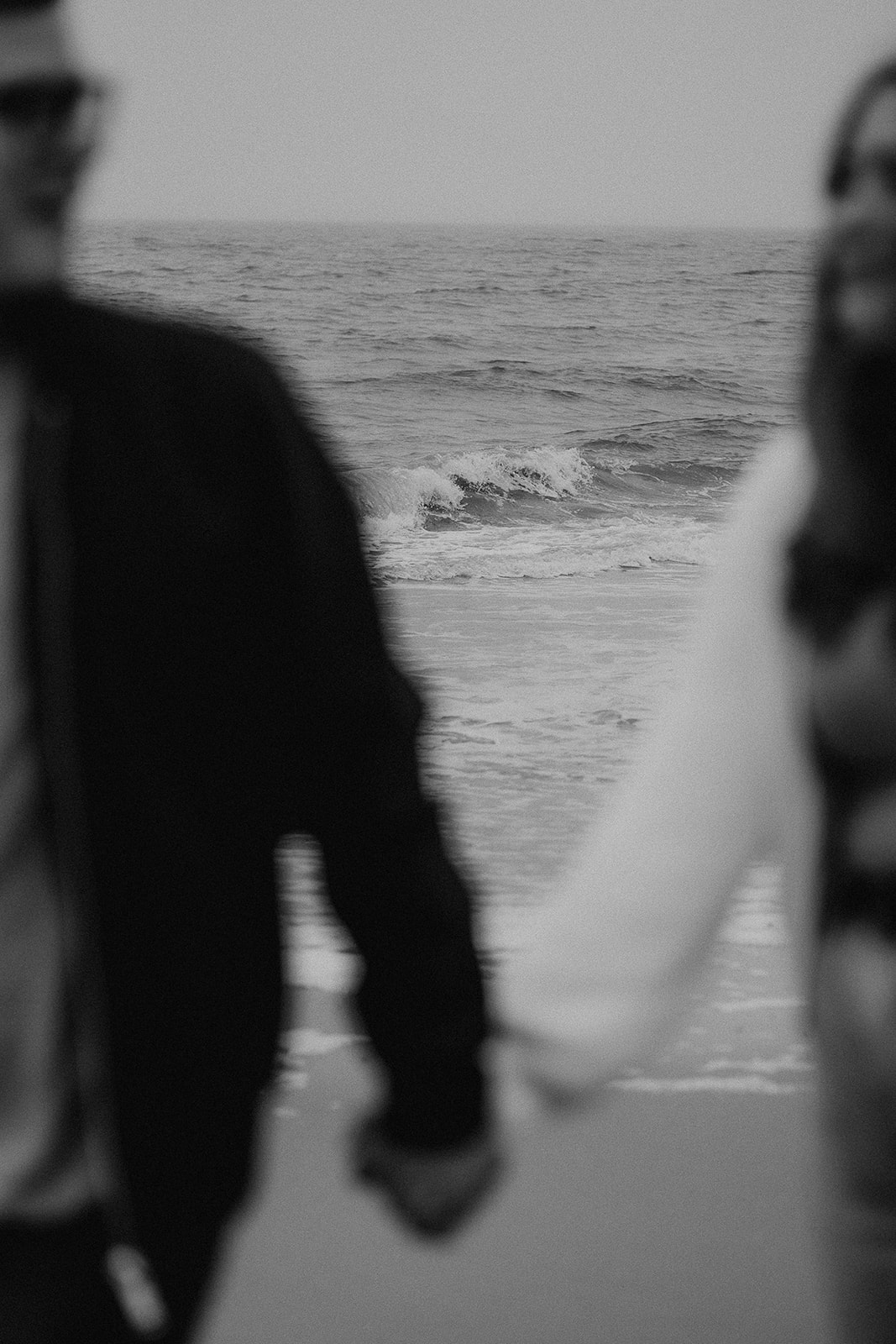 Waves lap against the shore between the arms of an engaged couple as they walk hand in hand along Highcliffe Beach. 