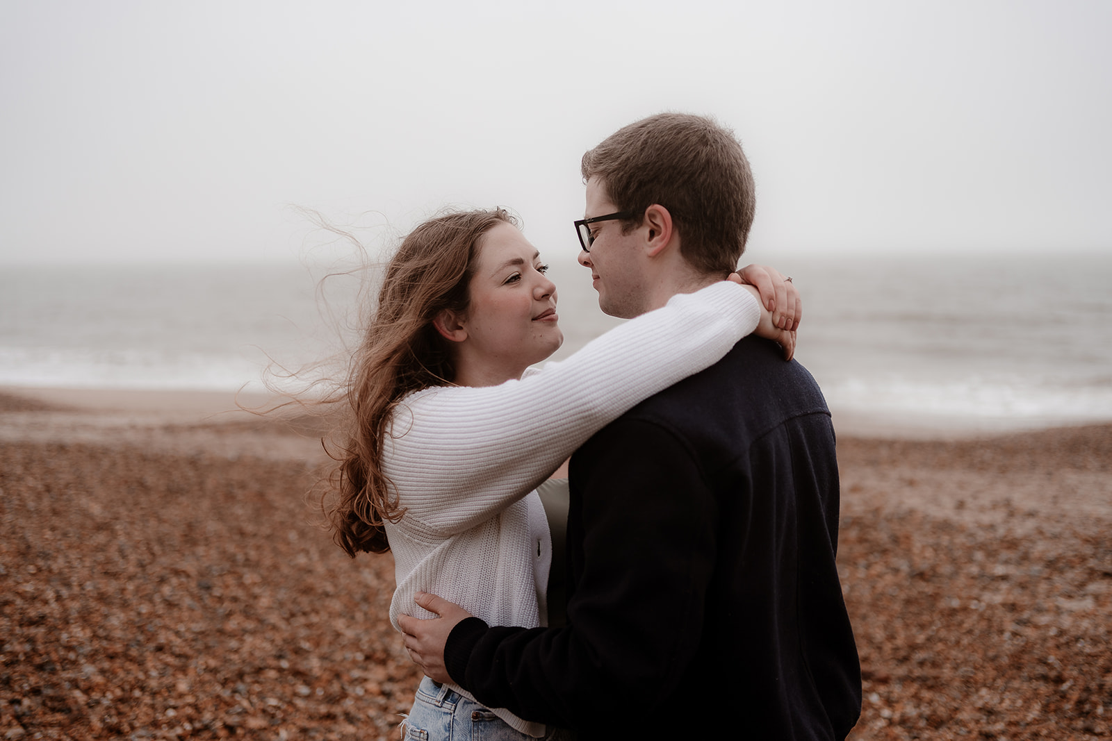 A woman wraps her arms around her fiance's neck at their Highcliffe Beach engagement photoshoot